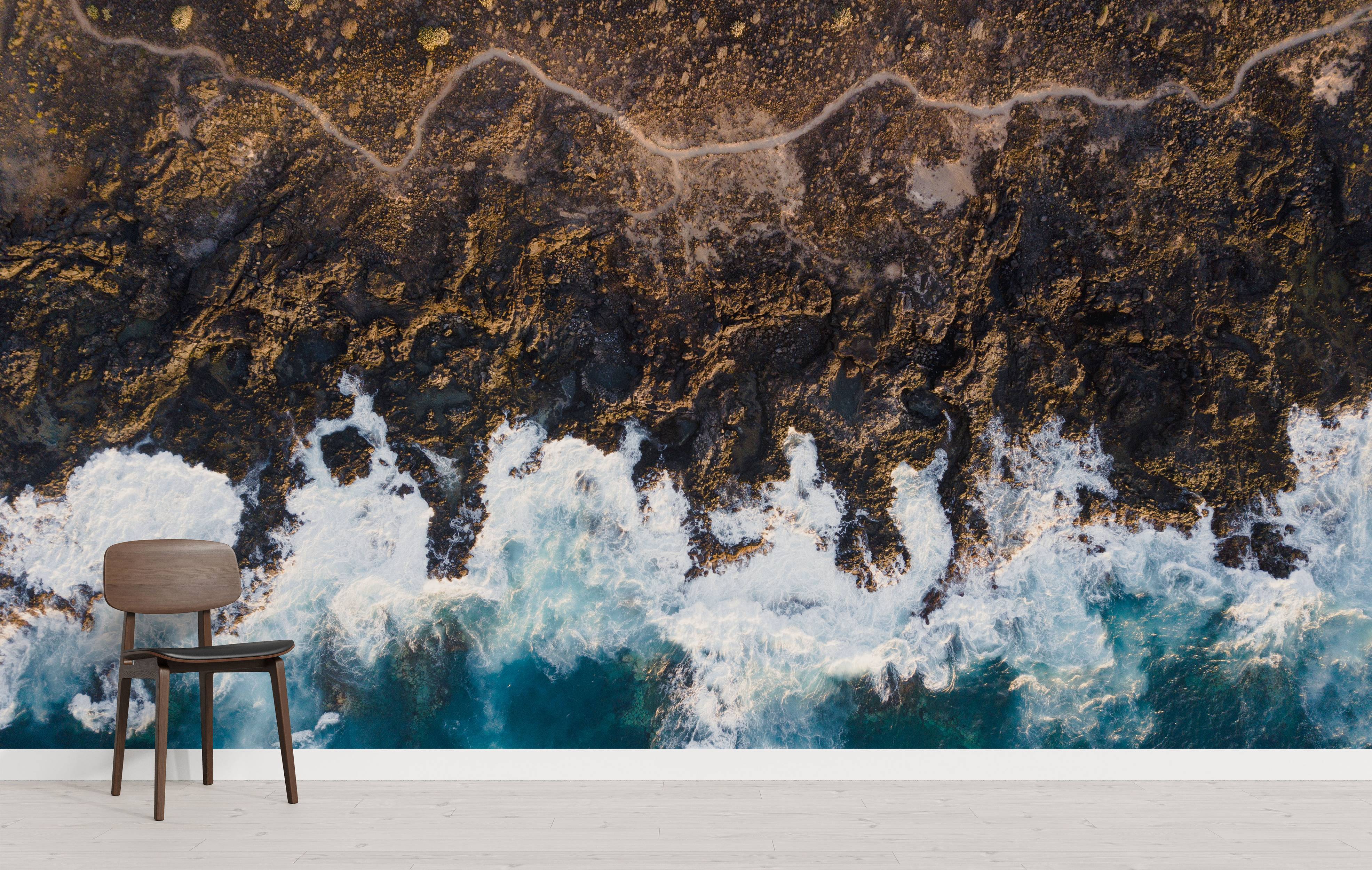 A dramatic aerial view mural of a rugged, rocky coastline meeting a turquoise ocean with large, crashing white waves.