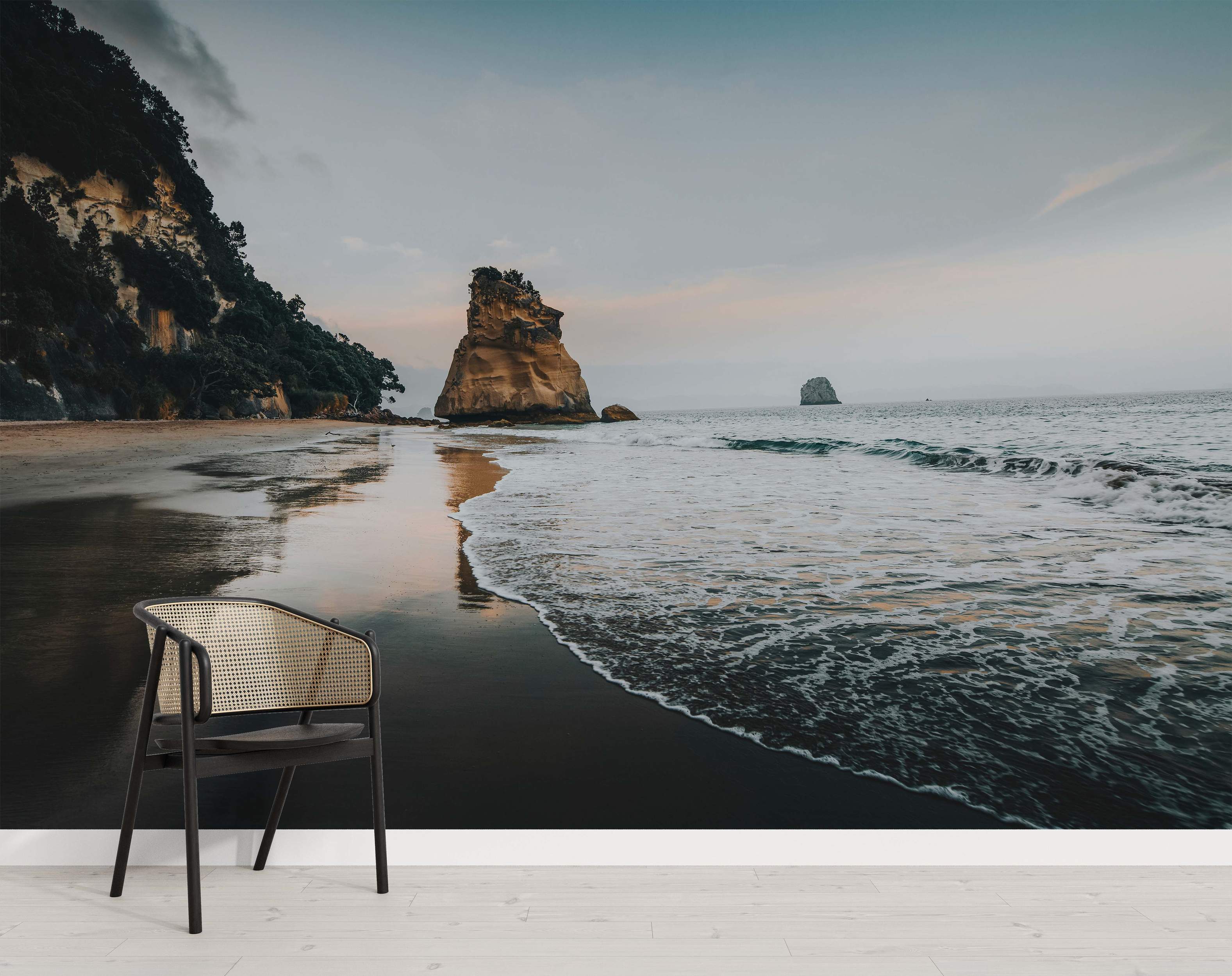 Mural showing a rocky beach with a large sea stack, dark sand, ocean waves, and a cloudy sky.