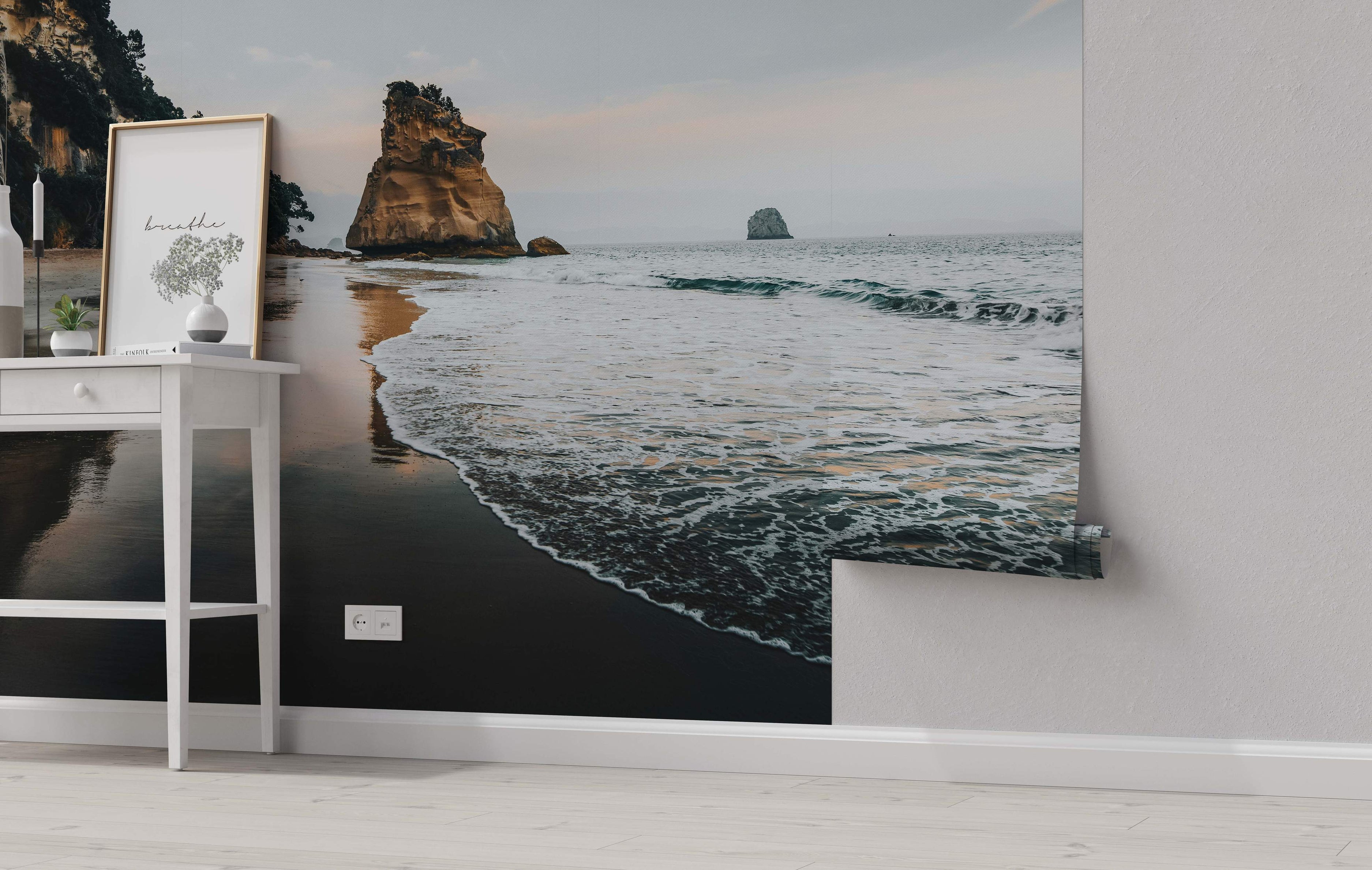 Mural depicting a serene beach scene at dusk with large rock formations, dark wet sand, and gentle ocean waves under a muted sky.