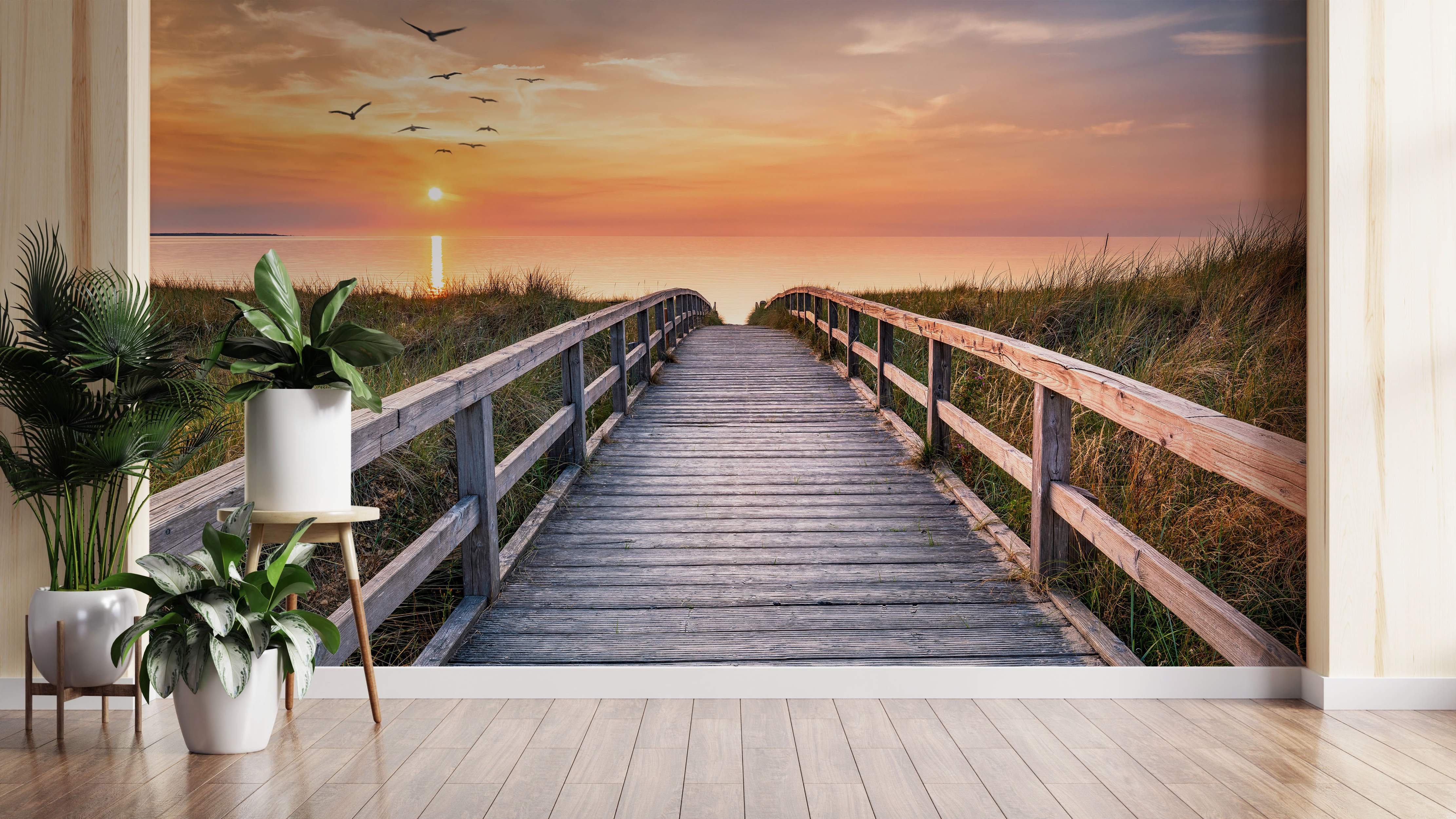 Mural depicting a wooden boardwalk through beach grass leading to the ocean during a vibrant orange sunset with birds flying.