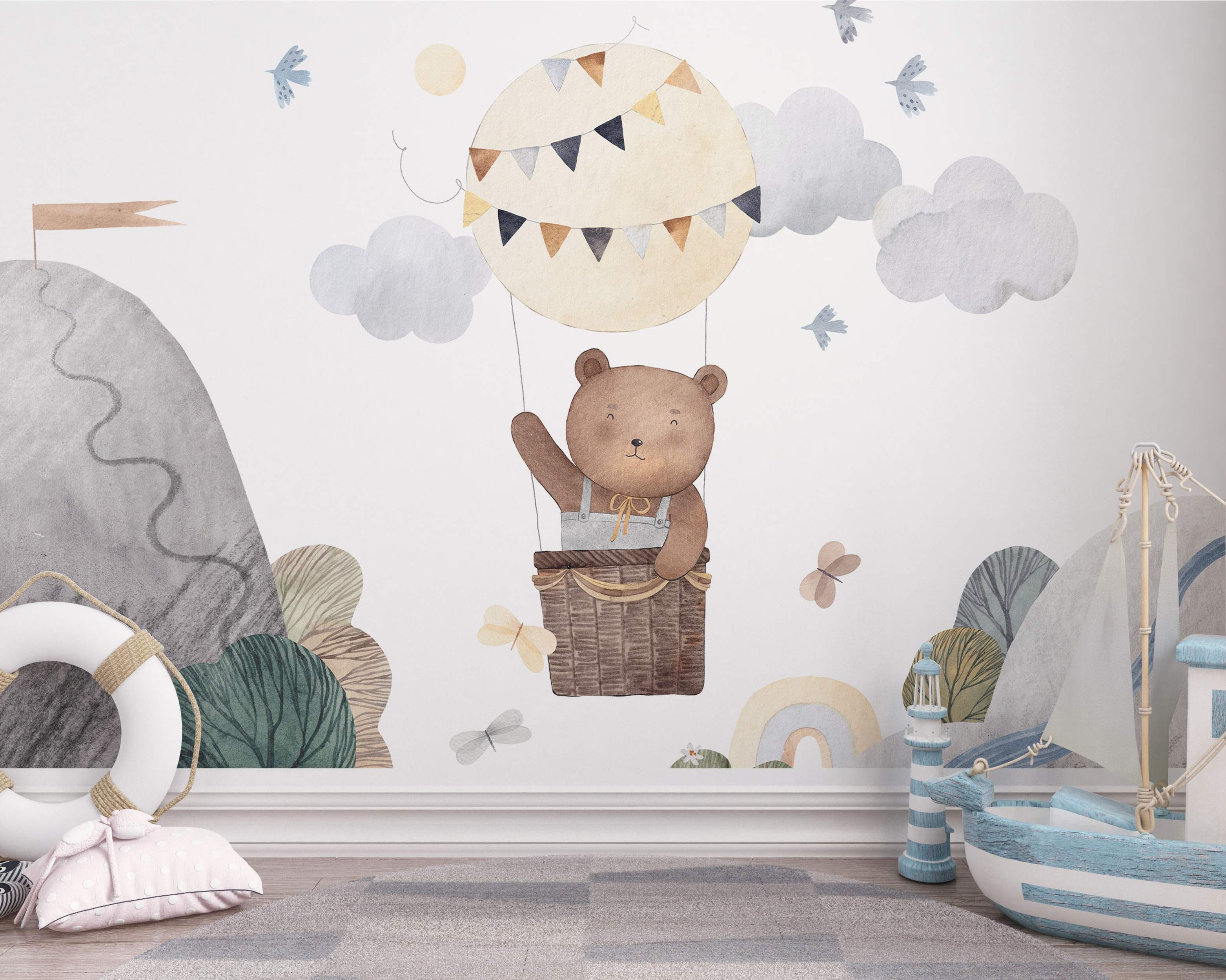 Watercolor mural featuring a cute brown bear in a hot air balloon amid blue-gray clouds, mountains, birds, and butterflies.