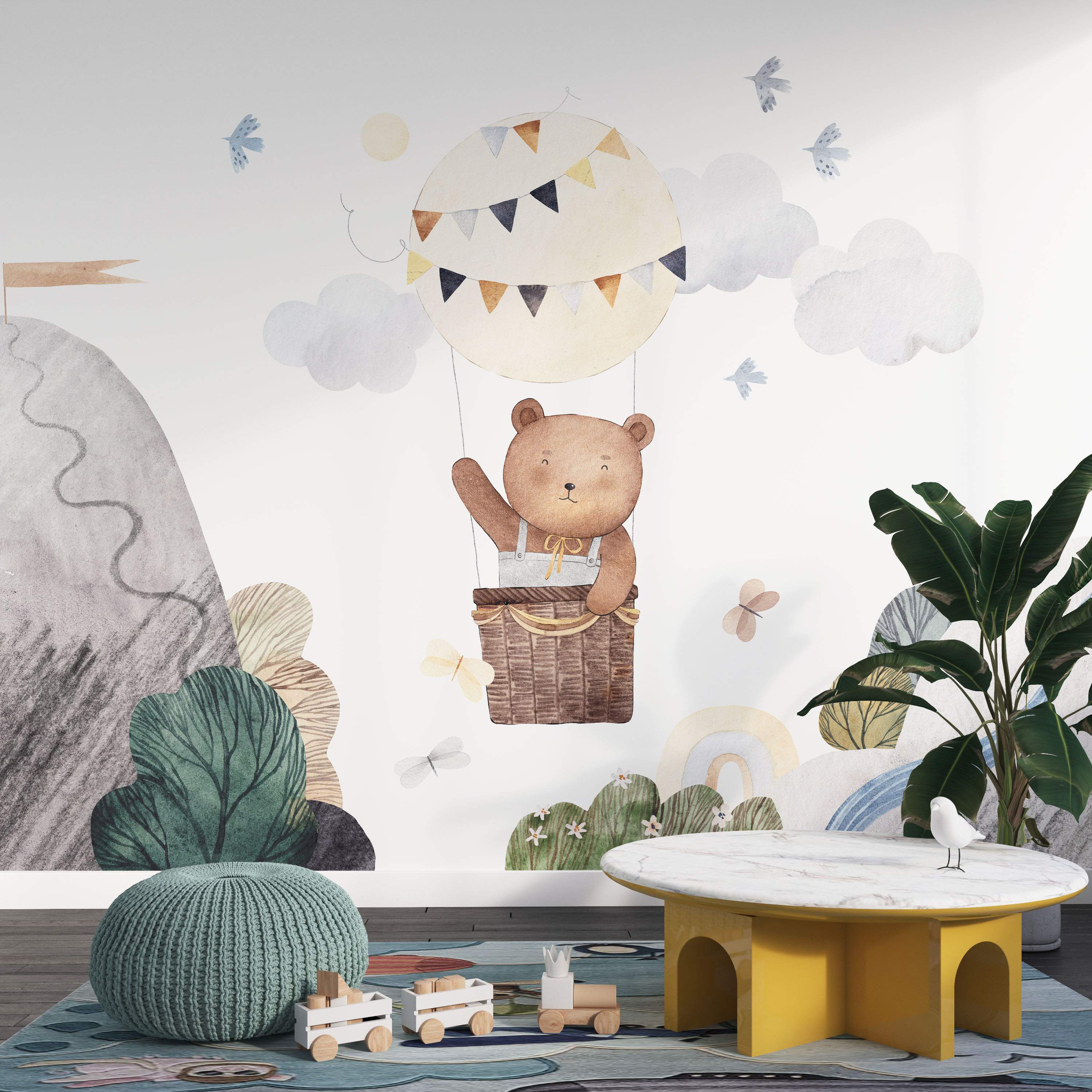 Watercolor mural featuring a friendly bear waving from a hot air balloon among clouds, birds, and gentle landscape elements.