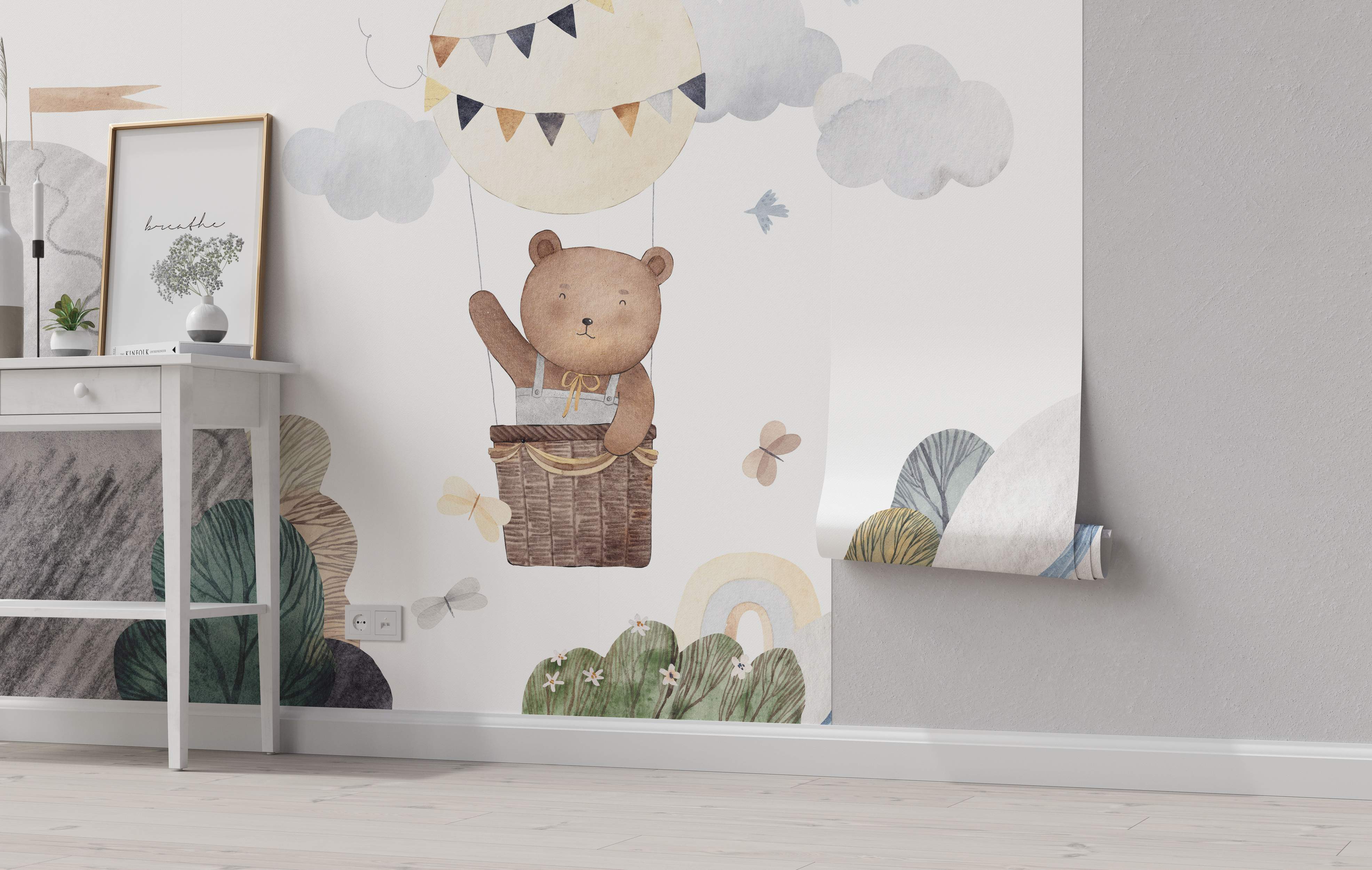 Watercolor mural featuring a cute brown bear waving from a hot air balloon basket, surrounded by clouds, butterflies, and plants.