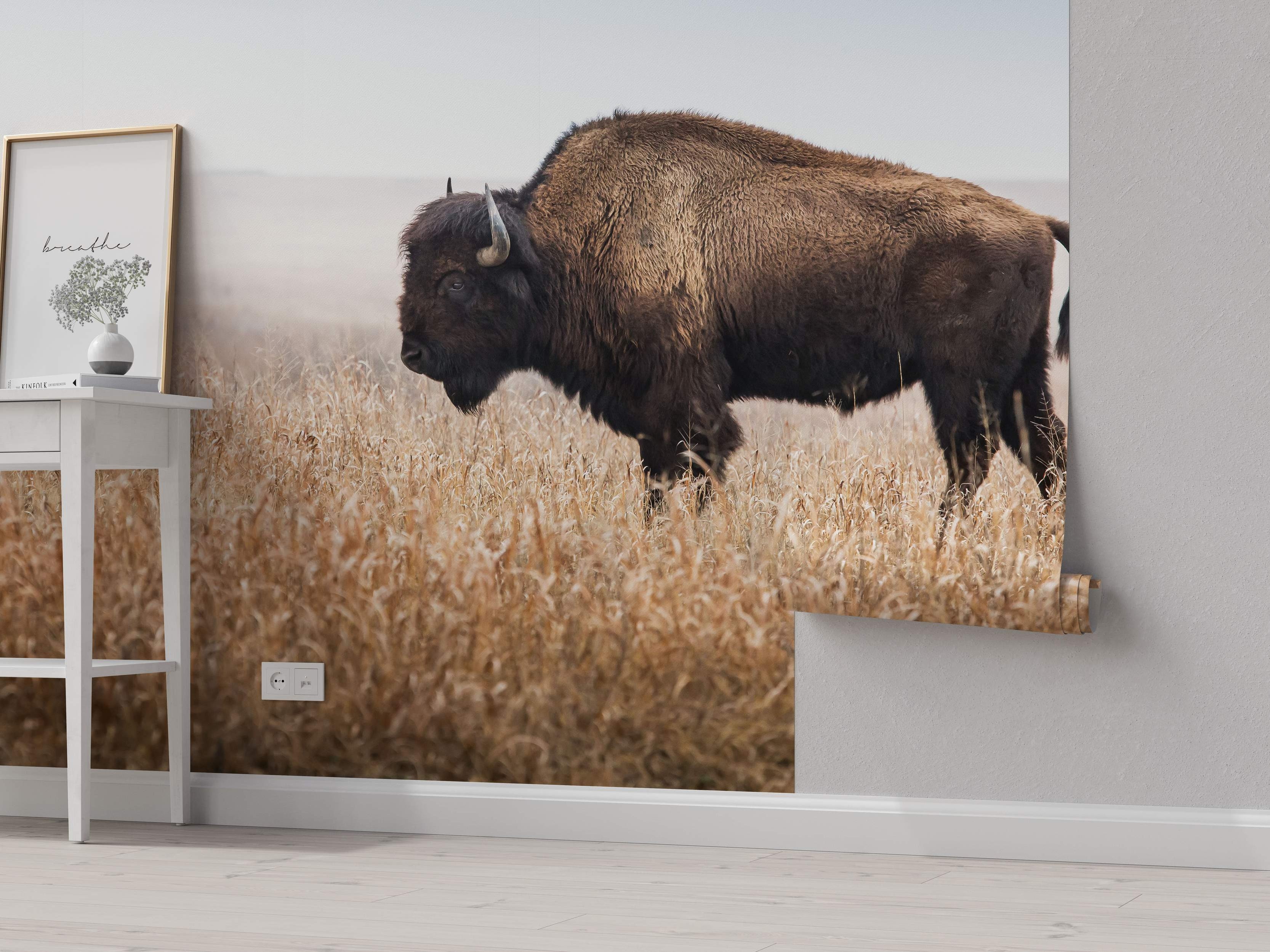 Photorealistic mural depicting a large brown bison standing in a field of tall golden grass beneath a pale, hazy sky.