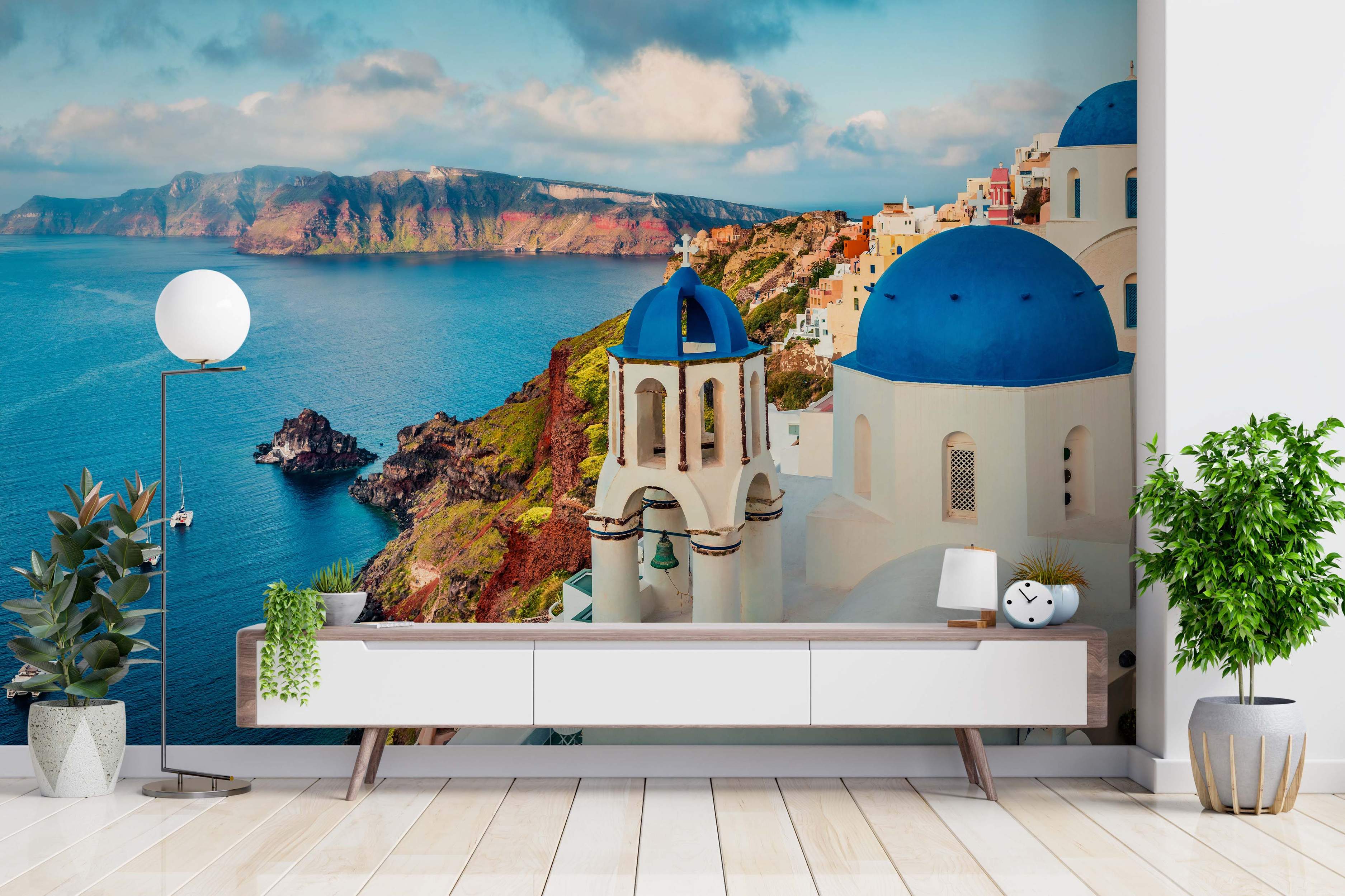 Scenic mural of Santorini with white buildings, blue domes, cliffs, and the blue sea under a partly cloudy sky.
