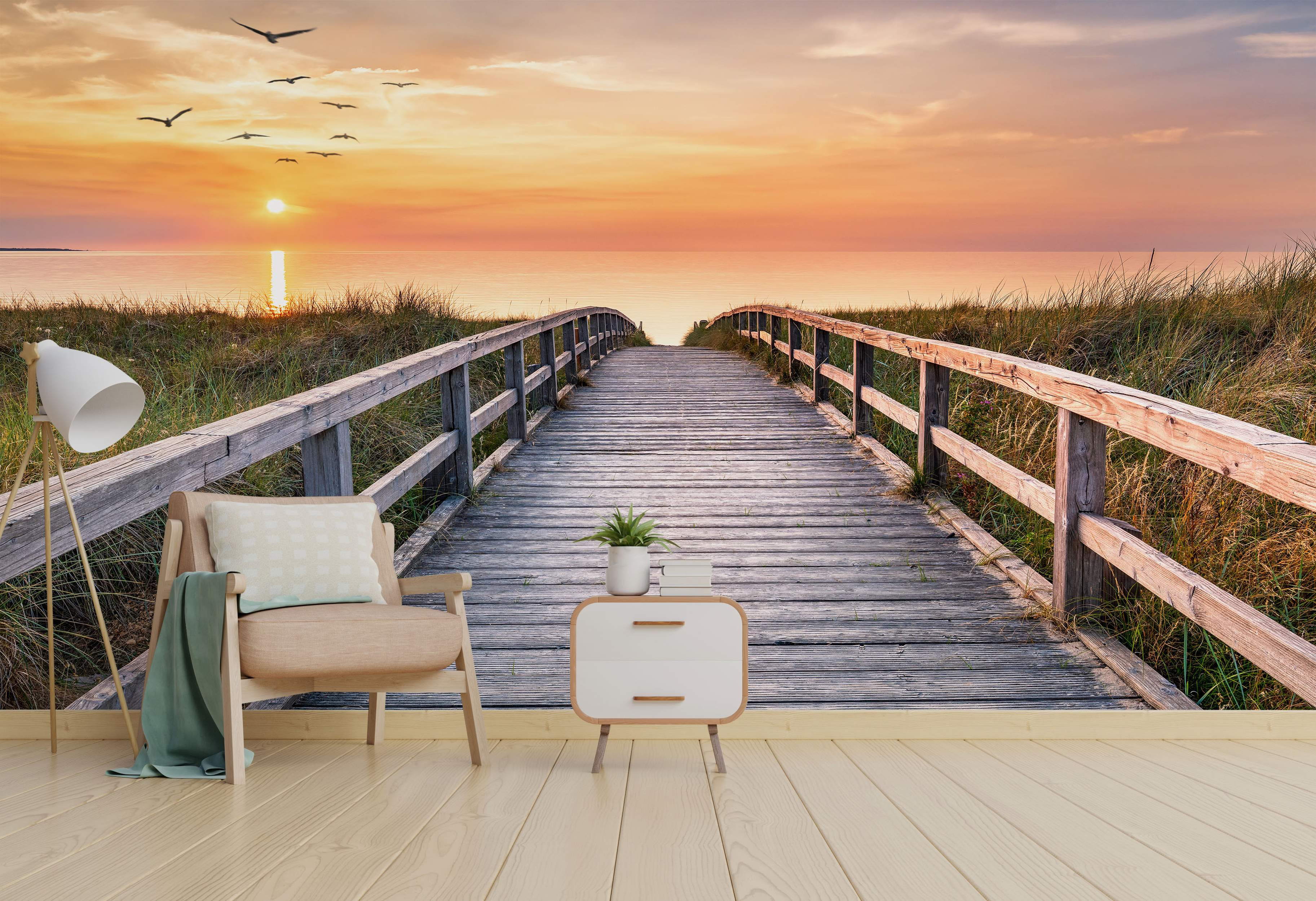 Mural depicting a wooden boardwalk leading to the ocean at sunset, with a warm orange and yellow sky and flying birds.