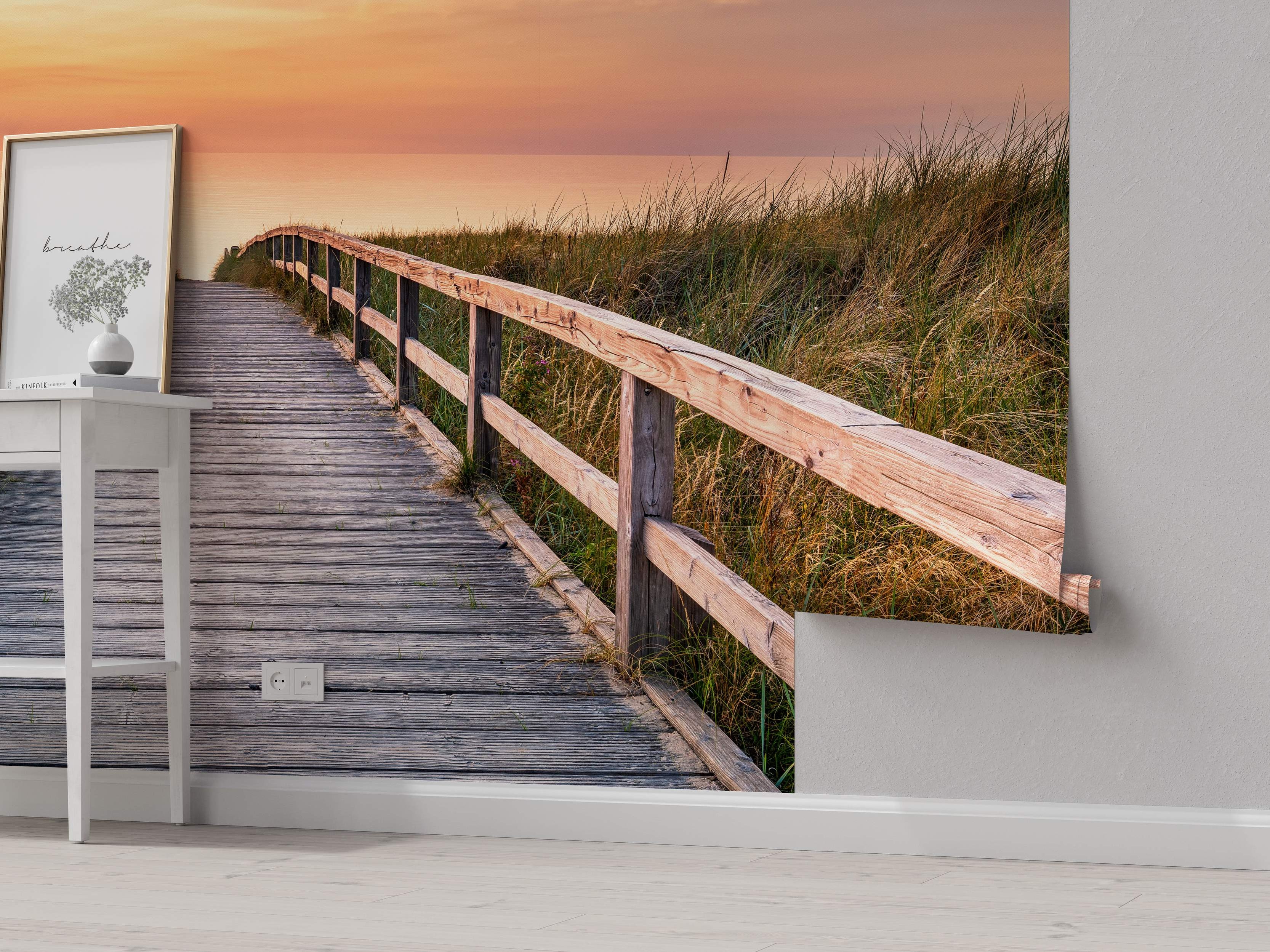 Scenic mural depicting a wooden boardwalk path through grassy dunes leading towards the ocean under a warm orange sunset sky.