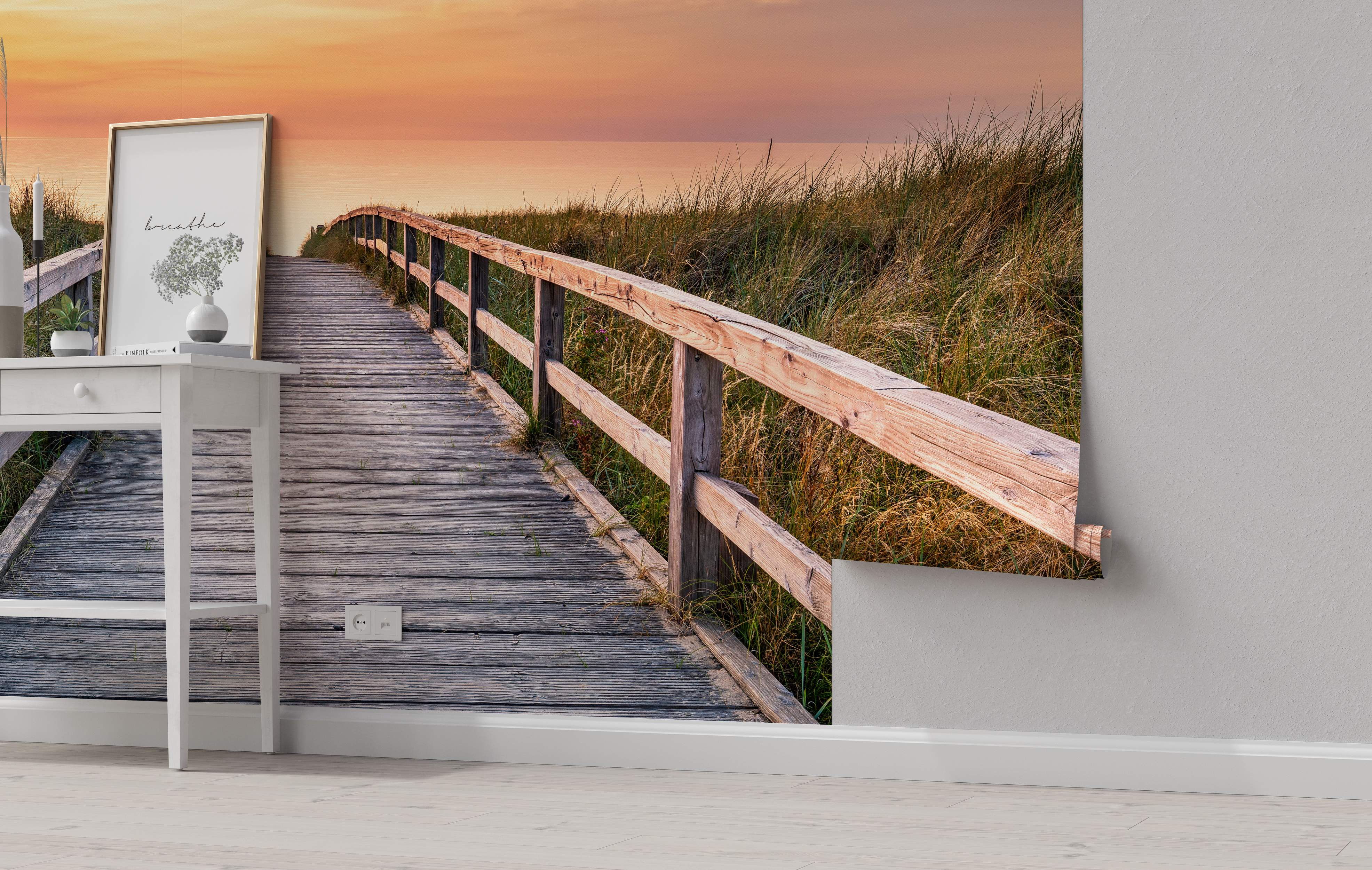 Scenic mural depicting a wooden boardwalk path through grassy dunes leading towards the ocean under a warm orange sunset sky.