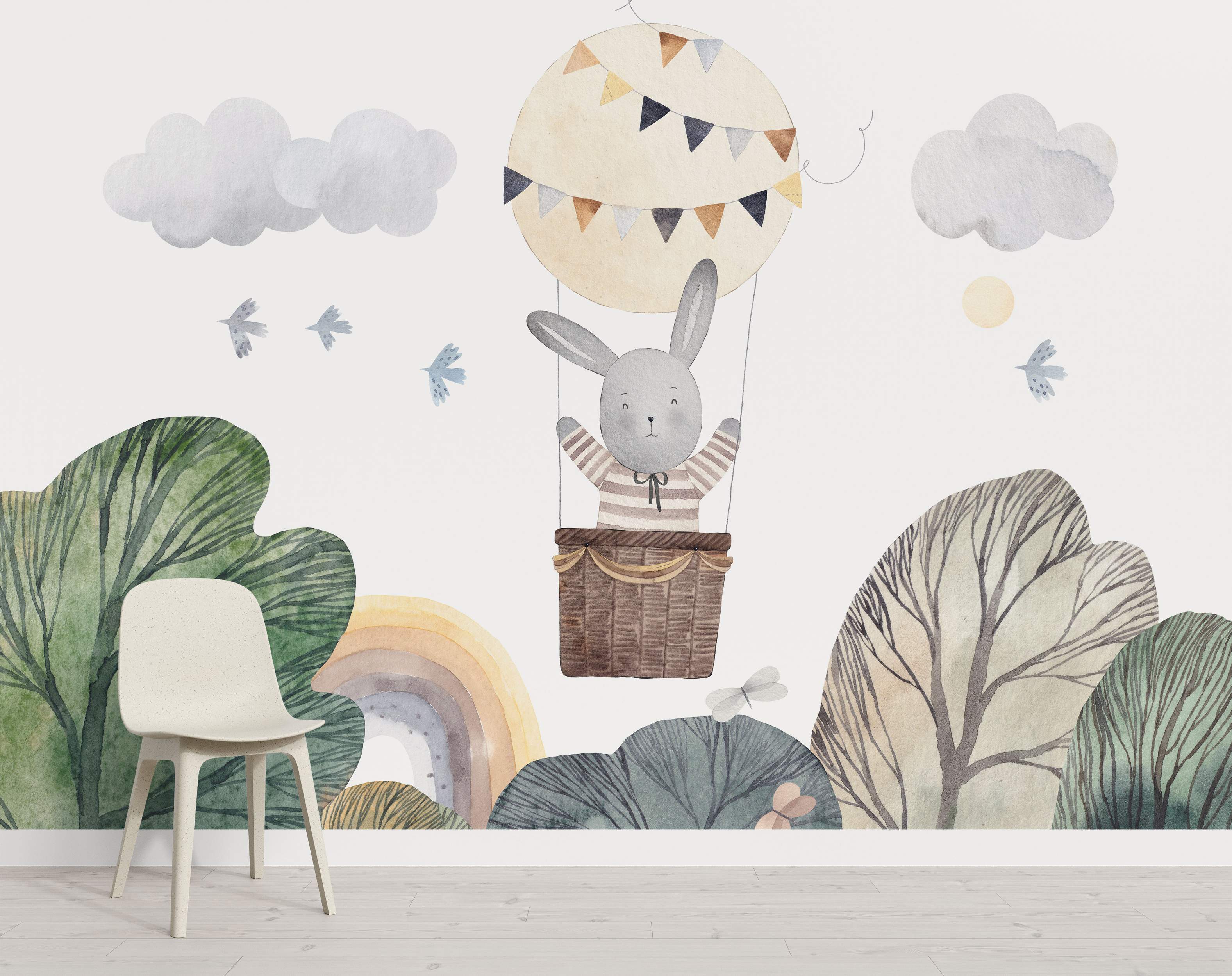 Watercolor mural featuring a gray bunny in a hot air balloon amid clouds, birds, trees, and a rainbow in soft pastel tones.