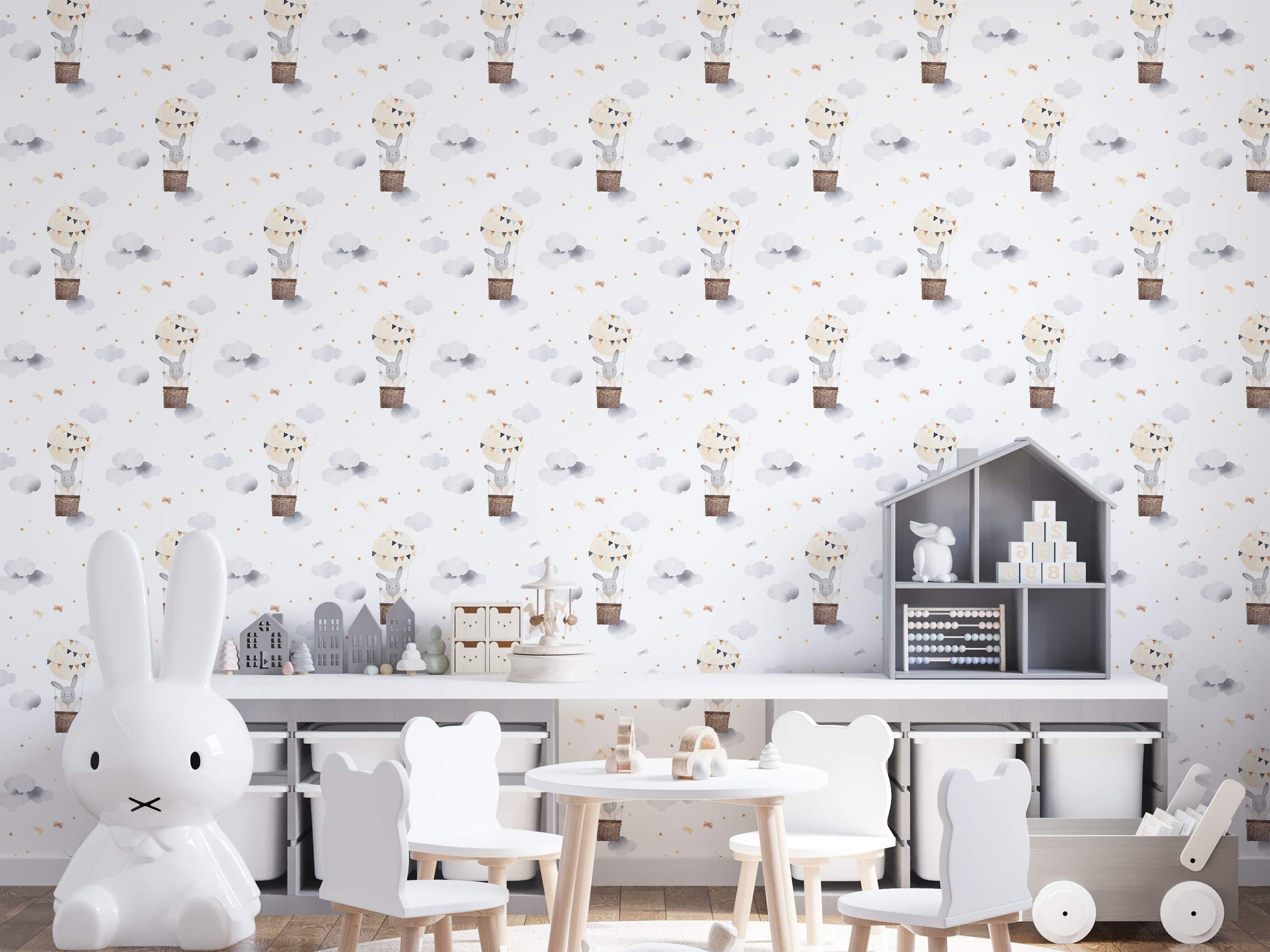 Watercolor wallpaper featuring gray bunnies in brown hot air balloons among gray clouds, gold stars, and beige bows on white.