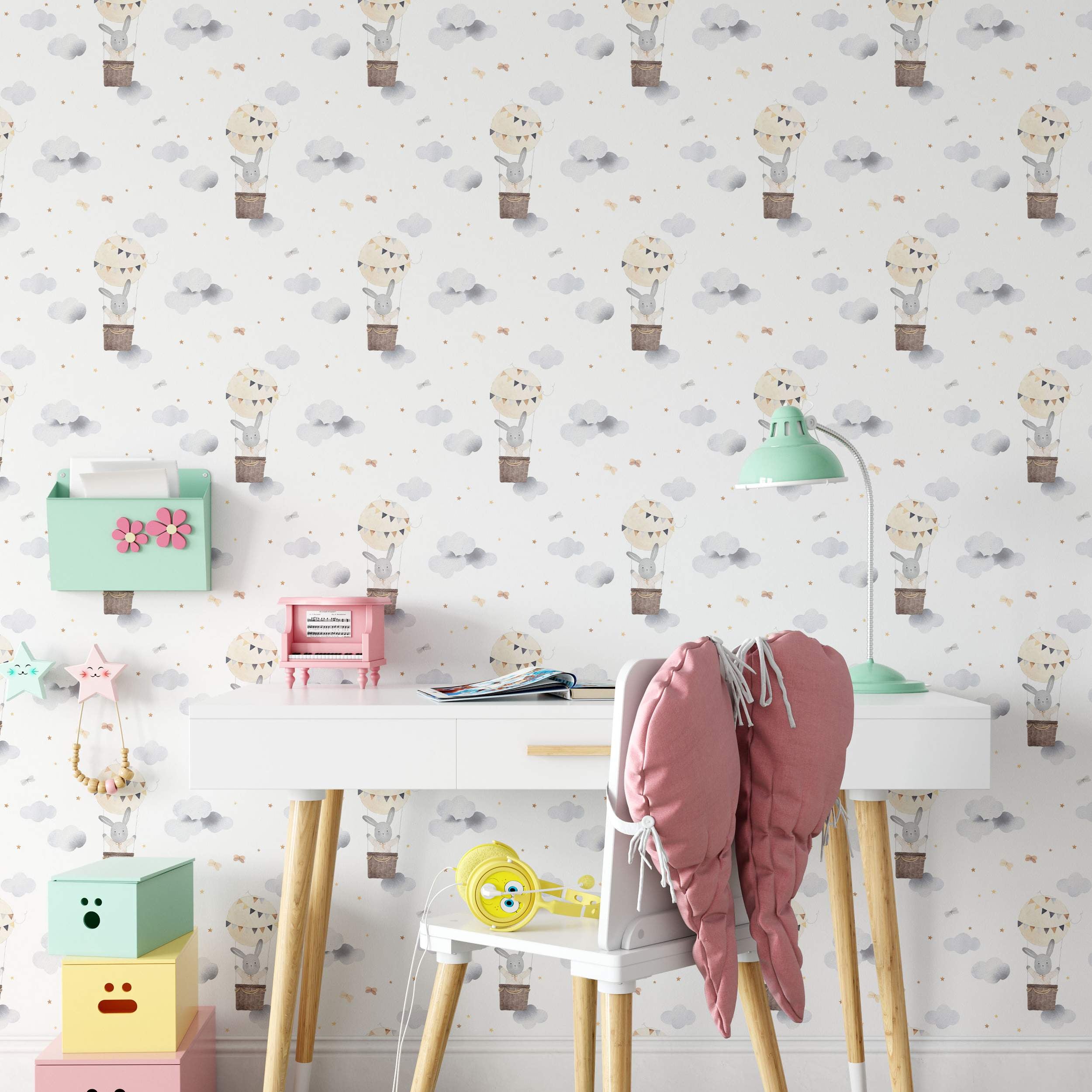 Wallpaper featuring a repeating pattern of watercolor bunnies in hot air balloons amongst grey clouds and gold stars on a white background.