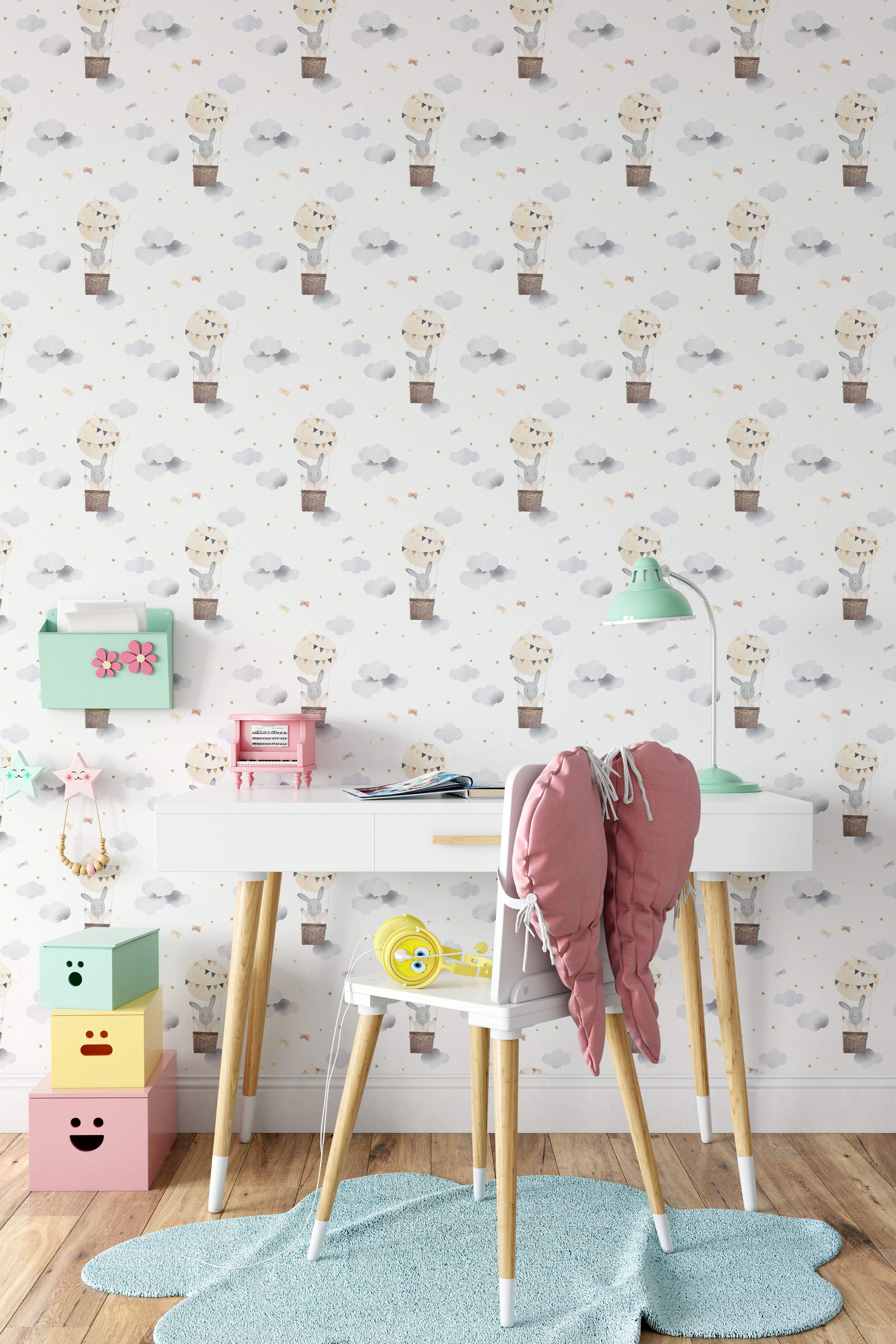 Wallpaper featuring a repeating pattern of watercolor bunnies in hot air balloons amongst grey clouds and gold stars on a white background.