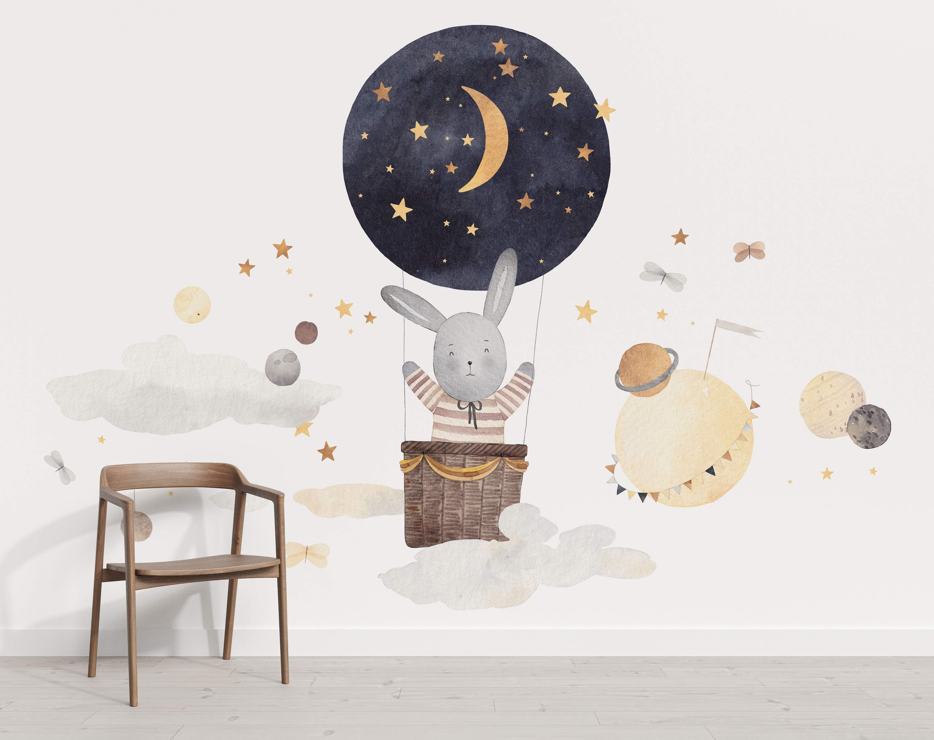 Watercolor mural featuring a gray bunny in a dark blue hot air balloon amid clouds, planets, and gold stars.