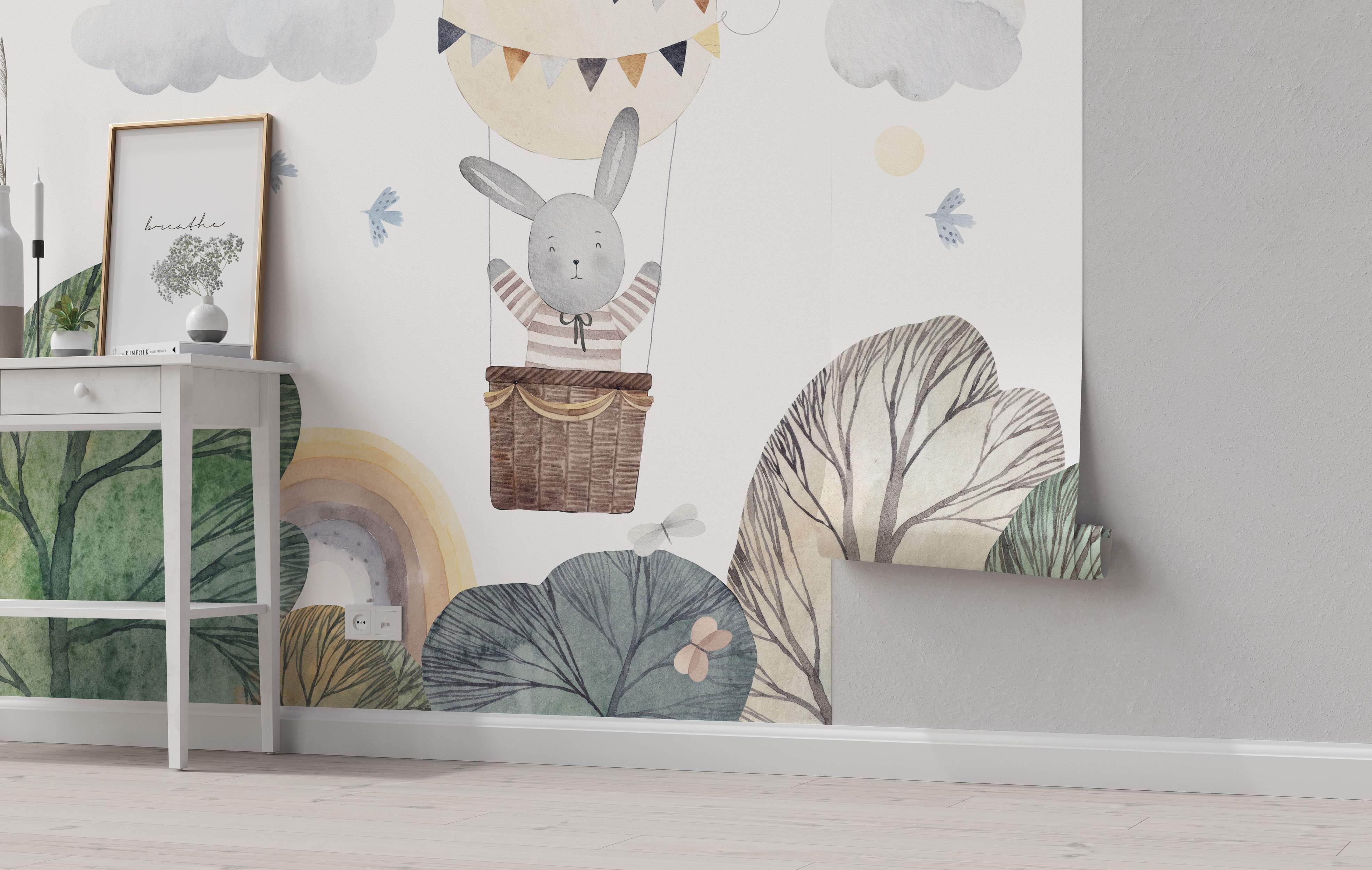 Watercolor mural featuring a gray bunny in a hot air balloon over trees and a rainbow, with clouds and birds. Soft colors.