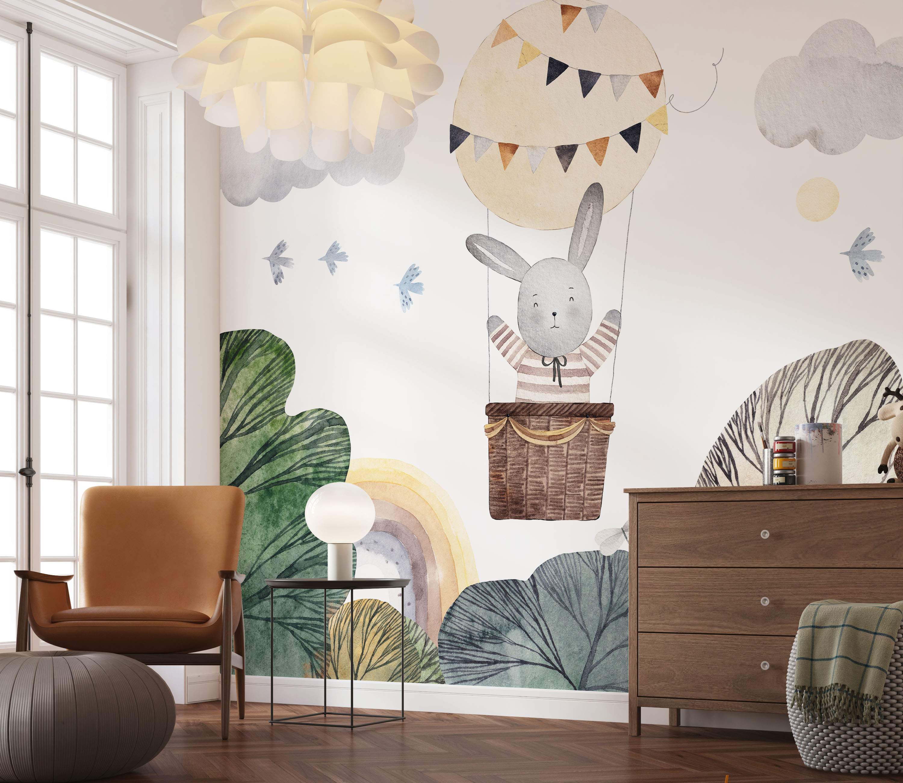 Watercolor mural of a gray bunny in a beige hot air balloon, with clouds, birds, rainbow, and trees in muted greens and browns.