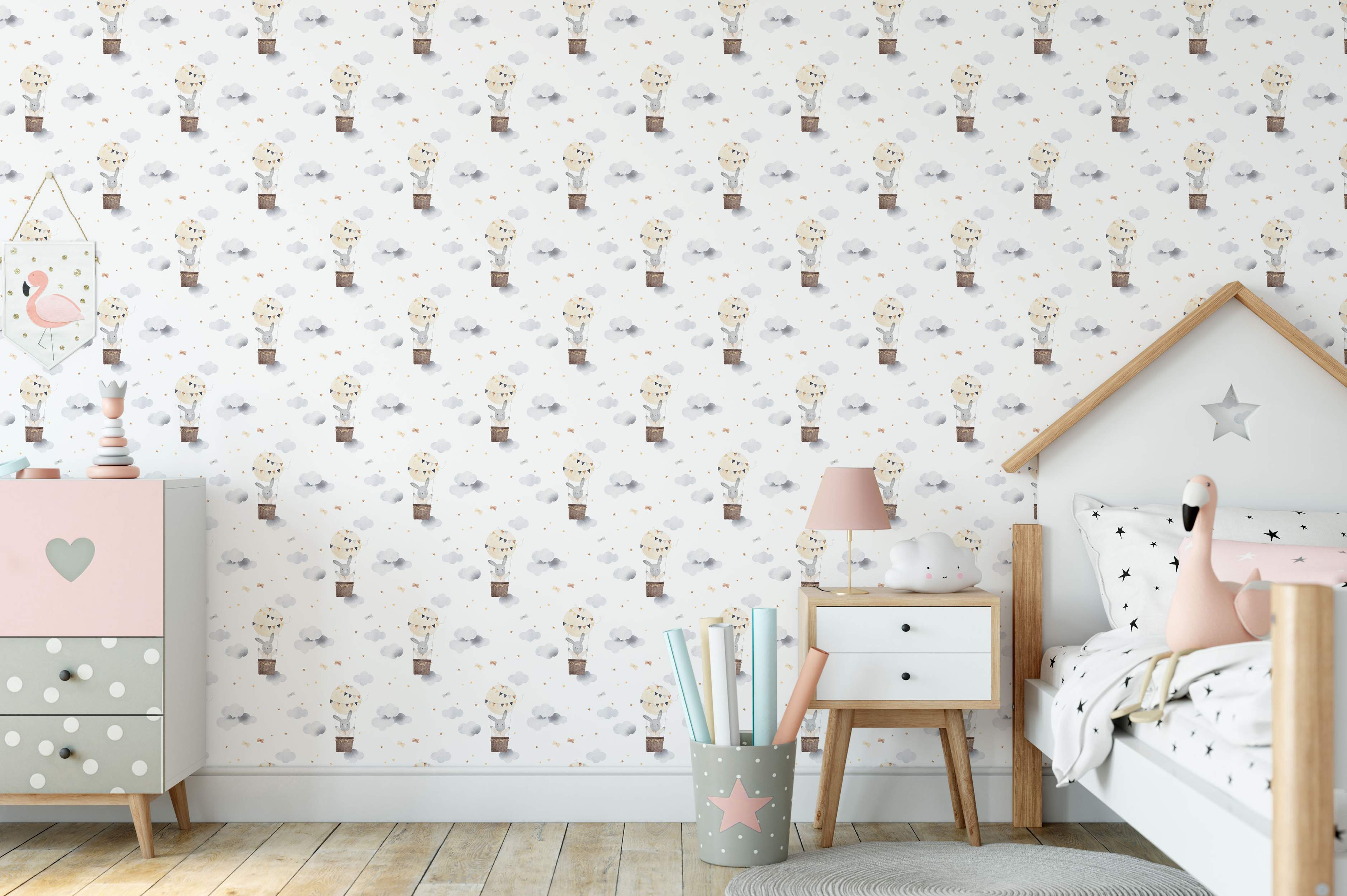 Wallpaper featuring a repeating pattern of watercolor bunnies in hot air balloons among gray clouds and gold stars on a white background.