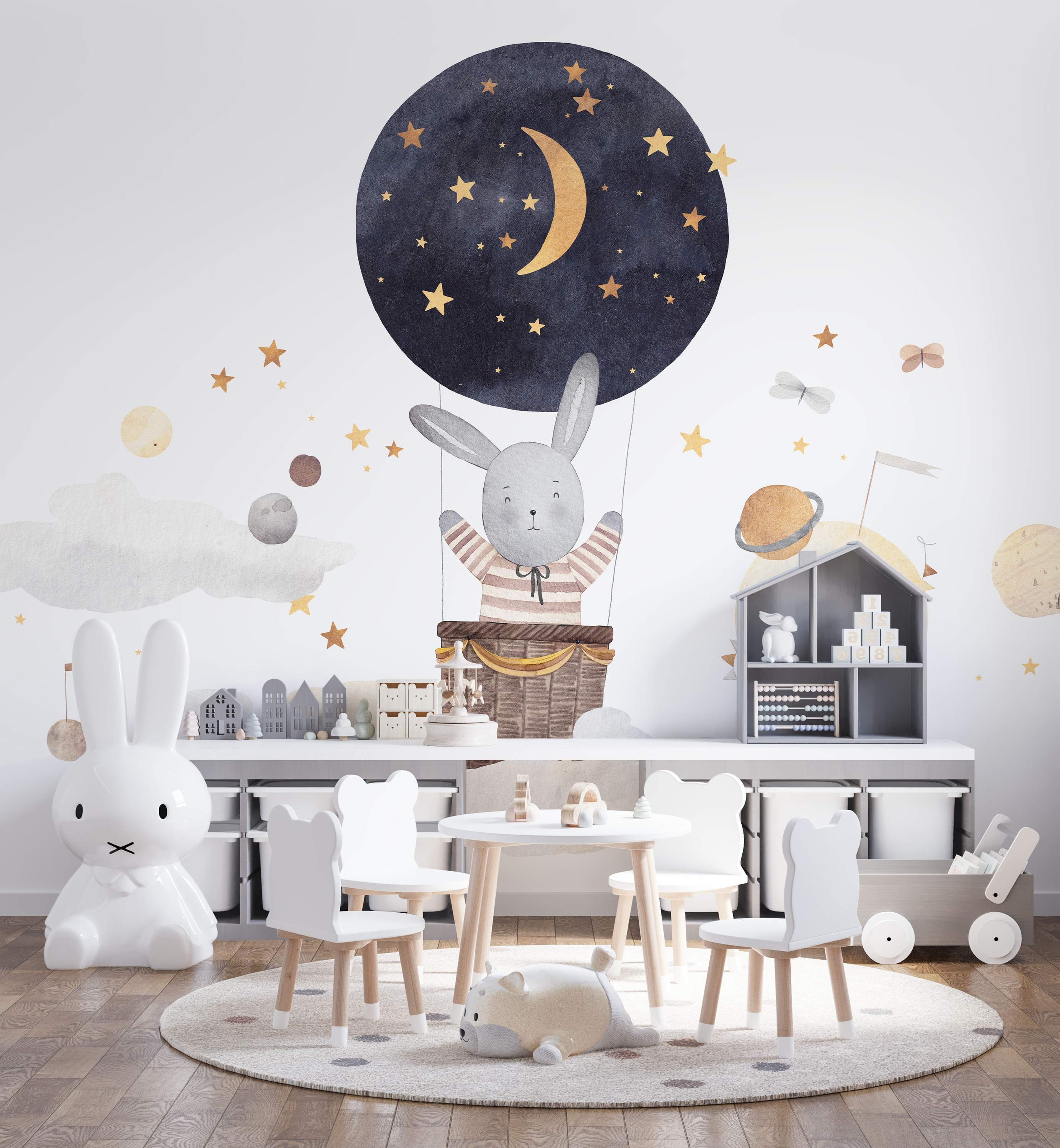 Watercolor mural featuring a gray bunny in a dark blue hot air balloon with gold stars and moon, surrounded by planets and stars.