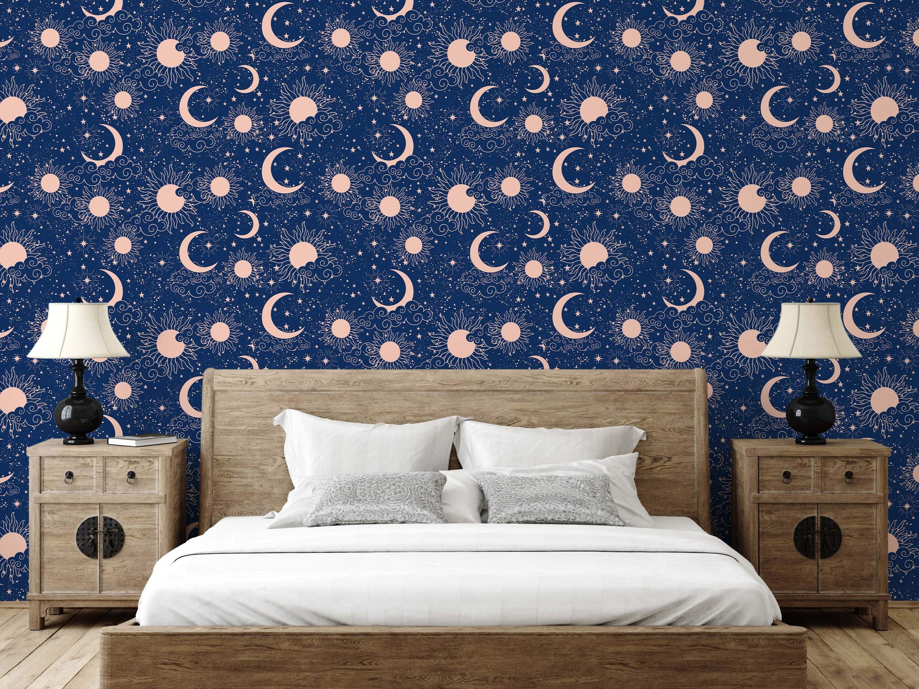 Celestial wallpaper with blush pink suns, crescent moons, stars, and clouds scattered on a dark navy blue background.