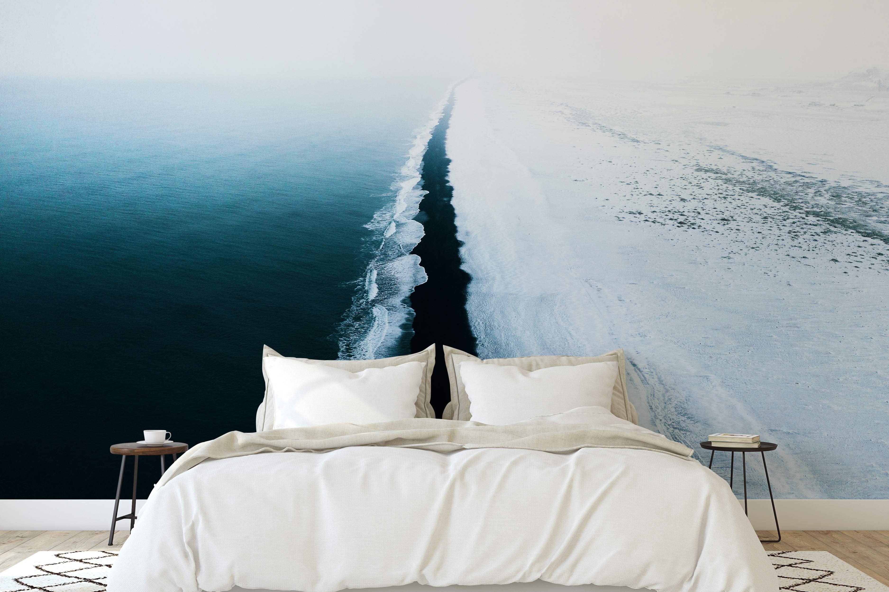 Atmospheric mural depicting an aerial view of a dark blue ocean meeting a black sand beach next to a snow-covered white landscape.