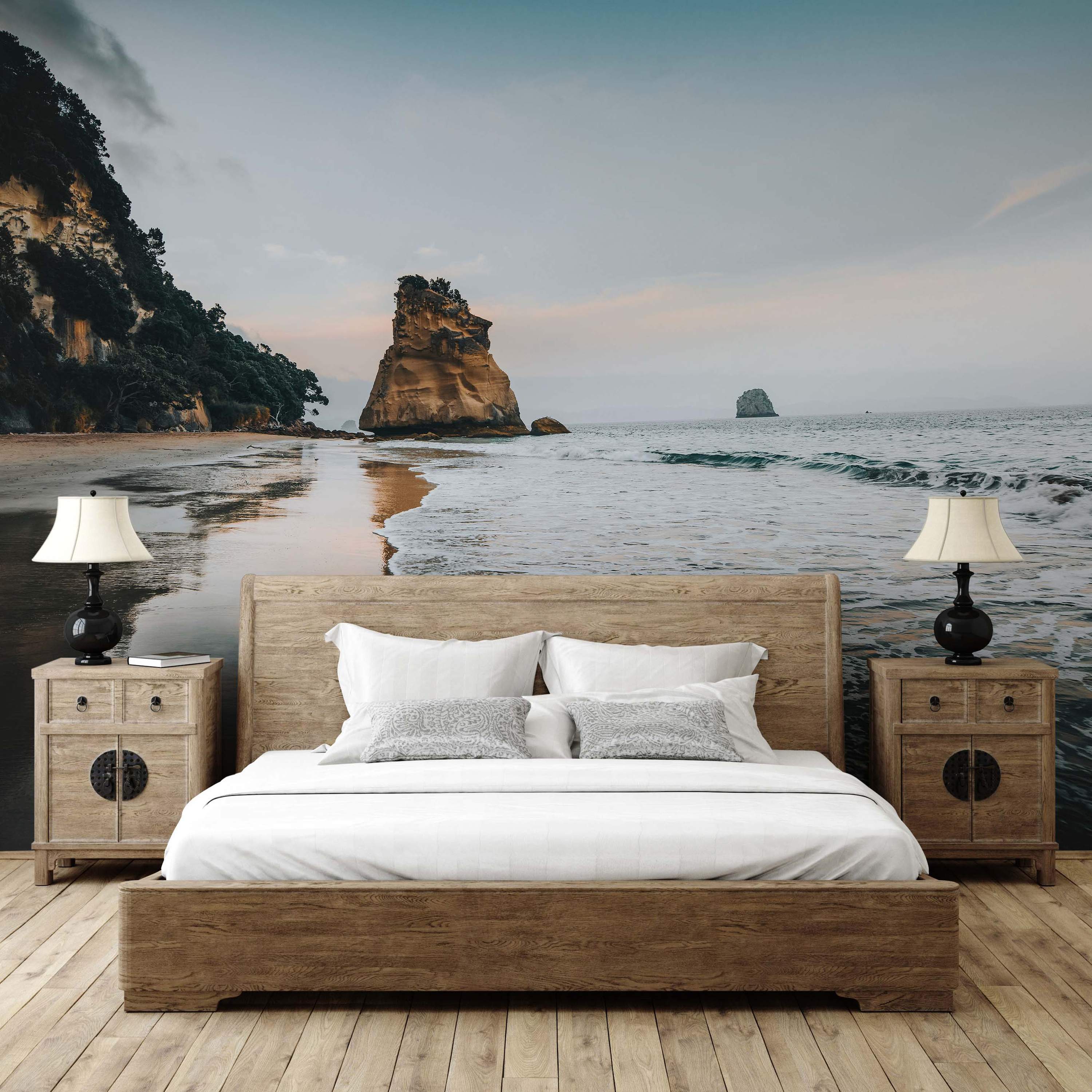 Photographic mural of a serene beach with a large rock formation in the water, cliffs, and a muted sky reflected in wet sand.