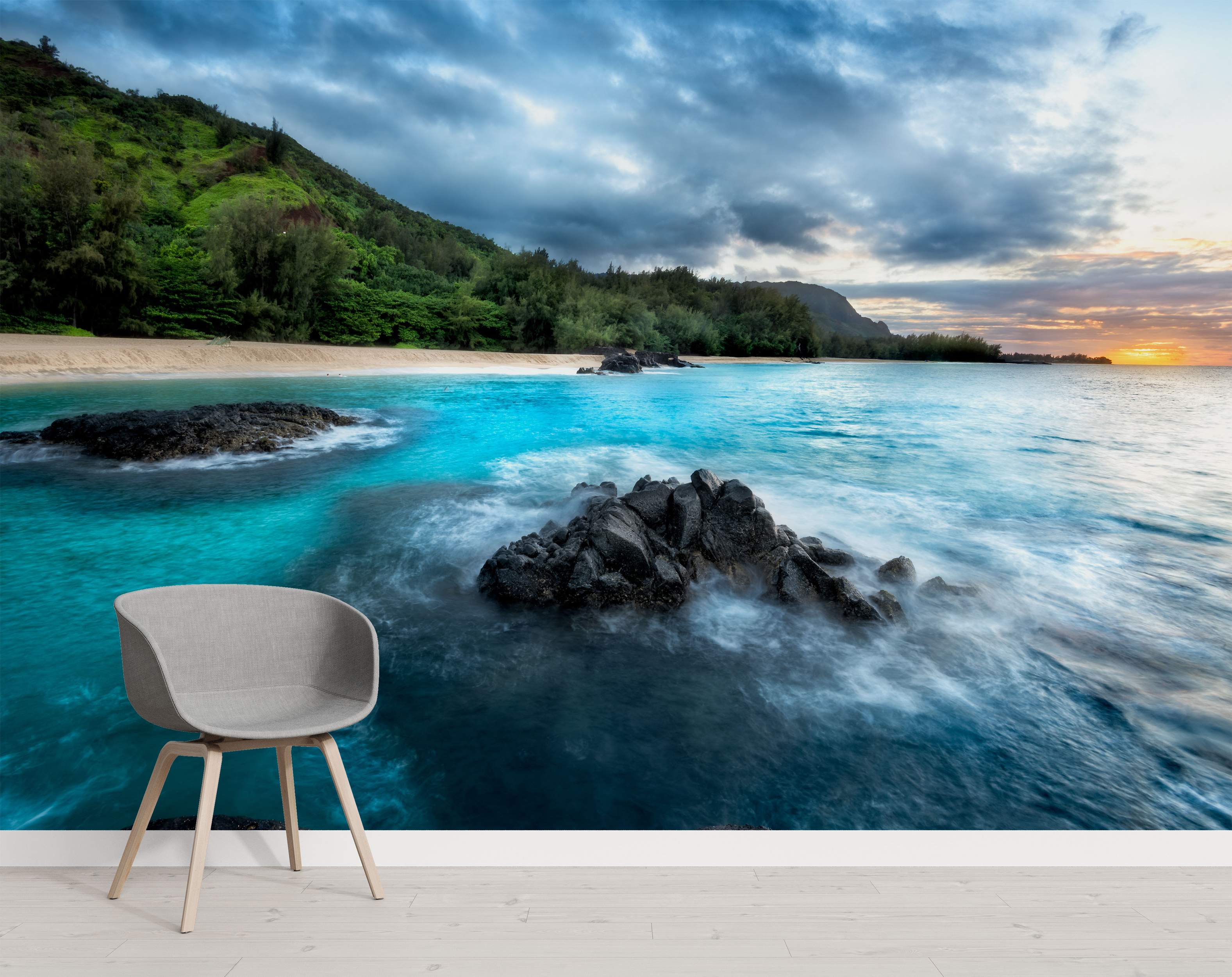 Photorealistic mural depicting a tropical coastline with vibrant blue water, dark rocks, a sandy beach, and green cliffs under a cloudy sky.