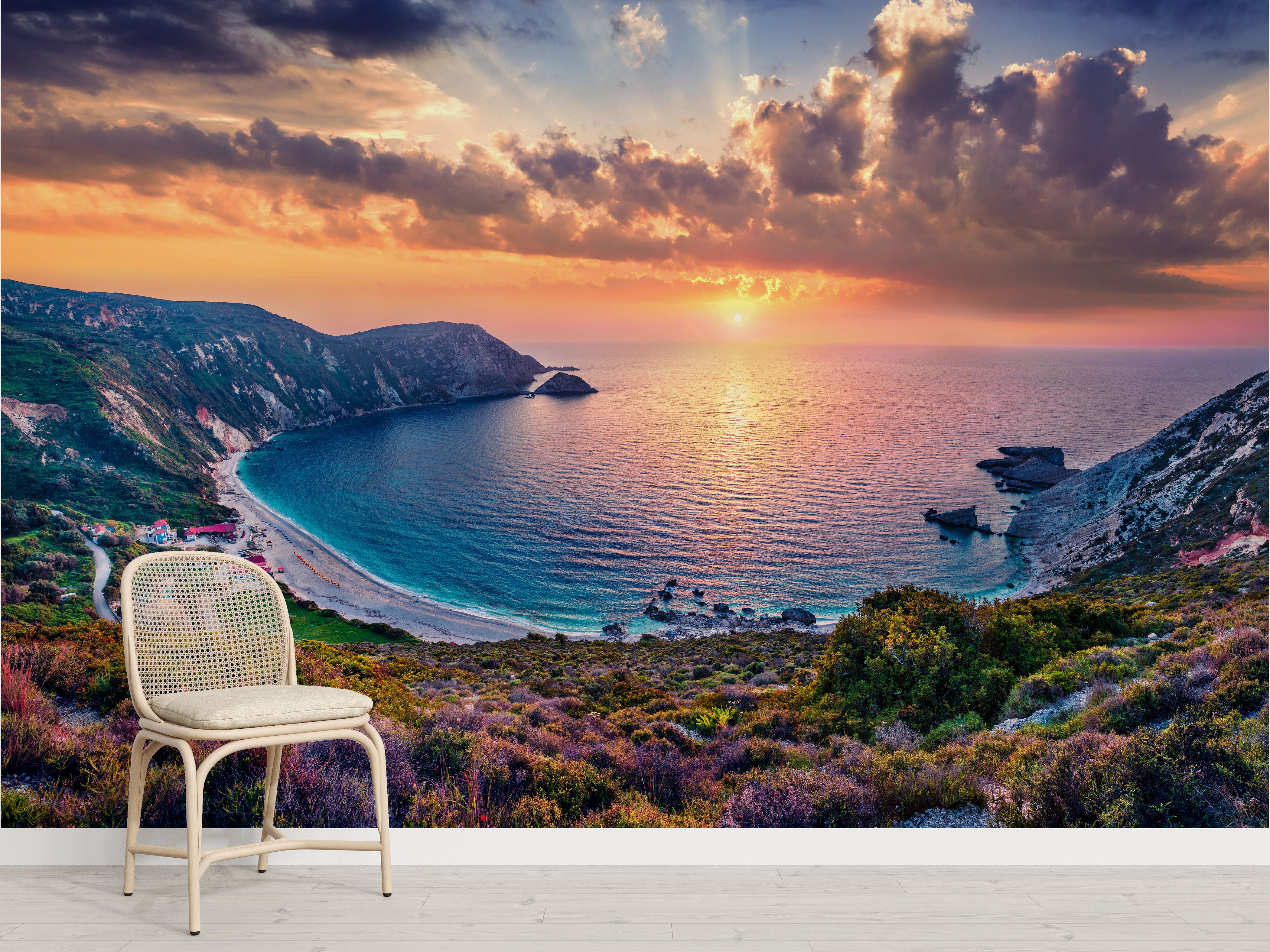 Mural depicting a dramatic coastal sunset over a blue bay, with orange clouds, steep cliffs, a beach, and colorful hills.