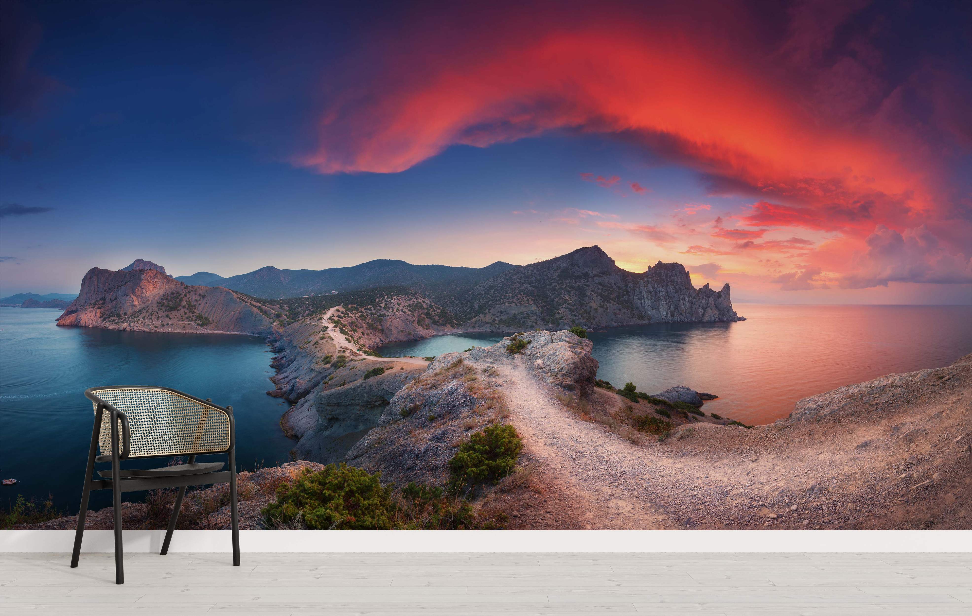 Photographic mural depicting a dramatic sunset over a rocky coastline, featuring red clouds, blue sea, and a cliffside path.
