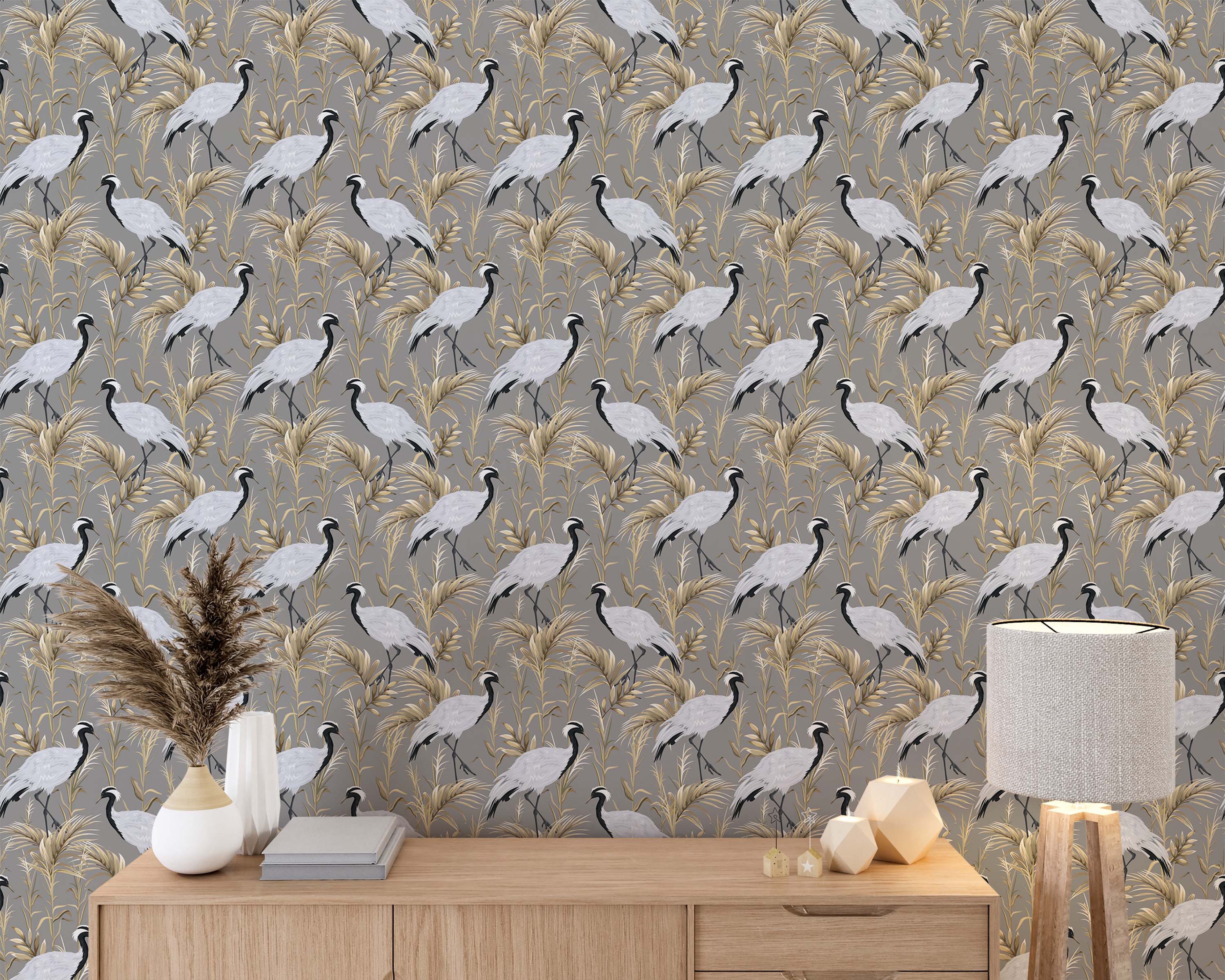 A repeating pattern wallpaper of elegant white and black cranes standing among beige and gold foliage on a gray background.