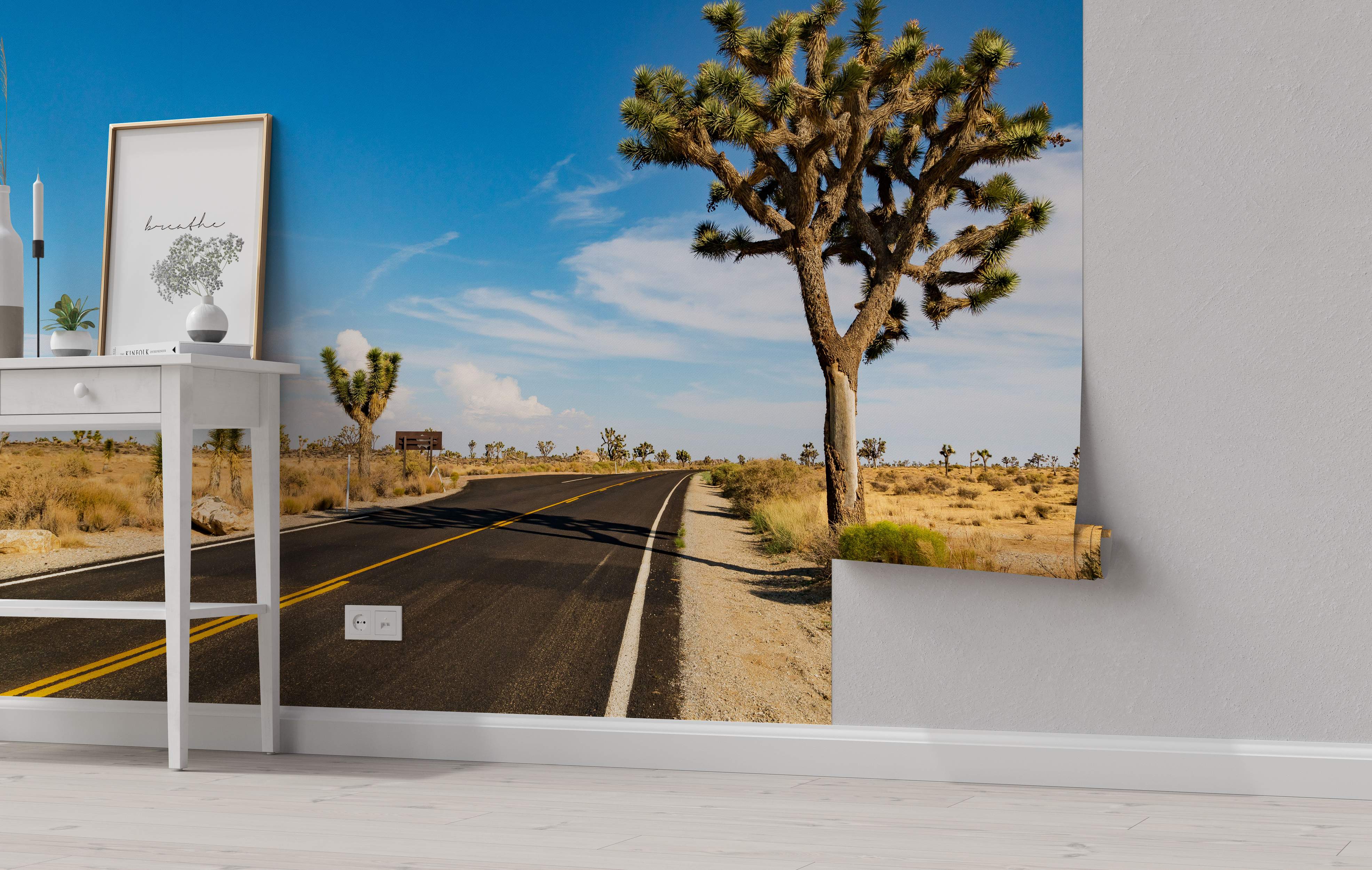 Photographic mural depicting a curving desert road flanked by Joshua trees under a bright blue sky with light clouds.