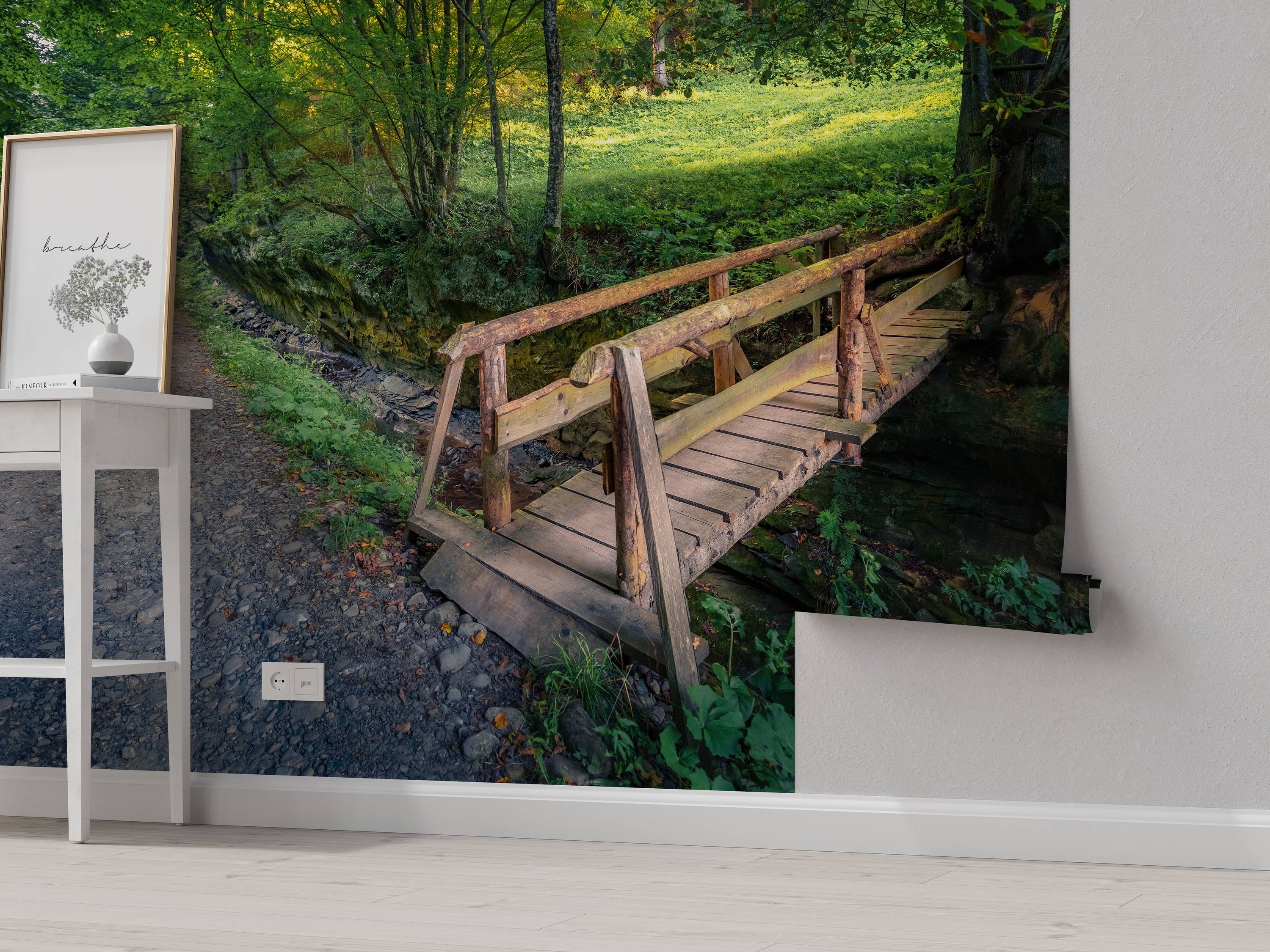 A scenic wall mural of a rustic wooden bridge crossing a rocky creek in a lush, sunlit green forest.