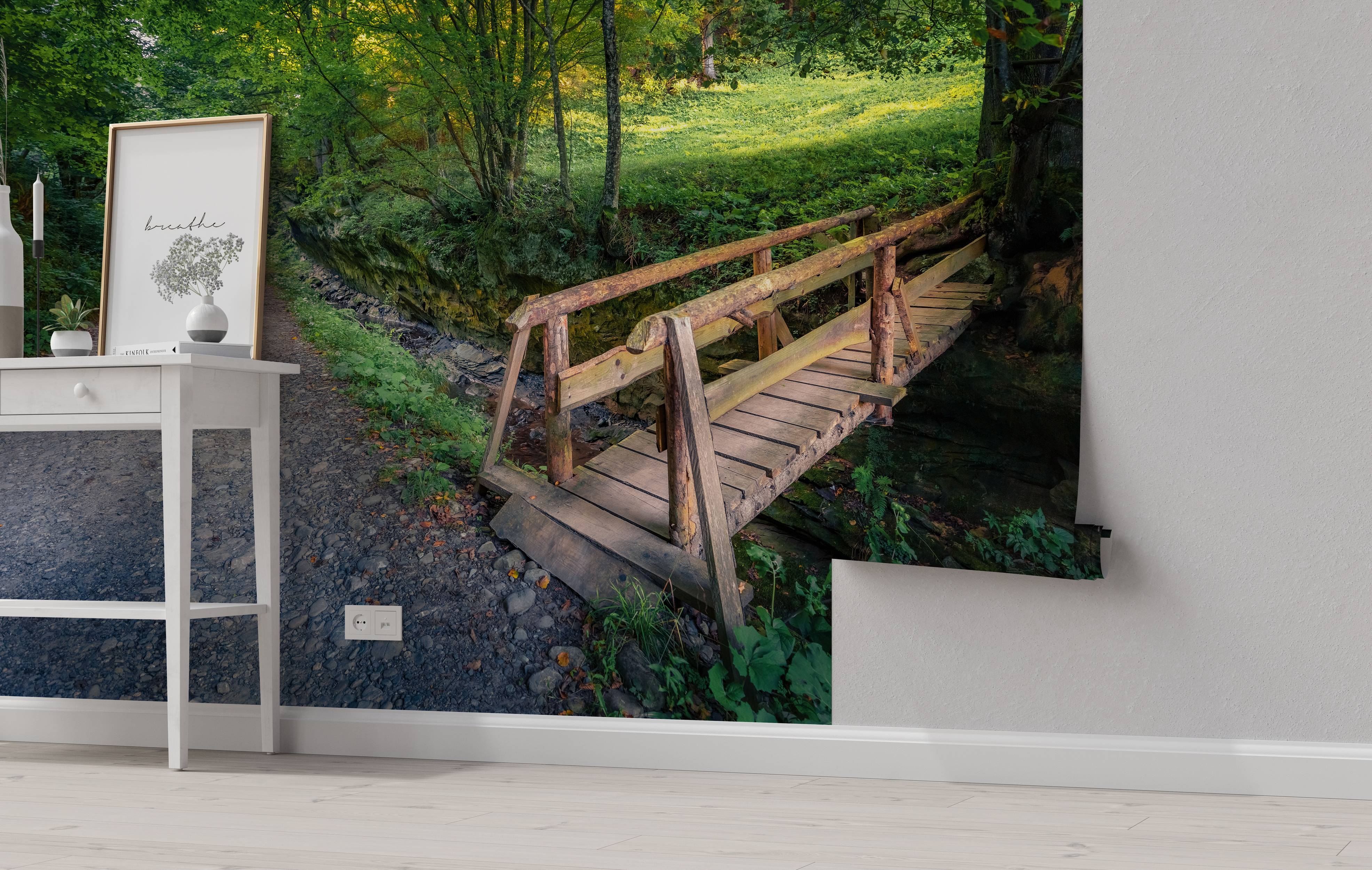 A scenic wall mural of a rustic wooden bridge crossing a rocky creek in a lush, sunlit green forest.
