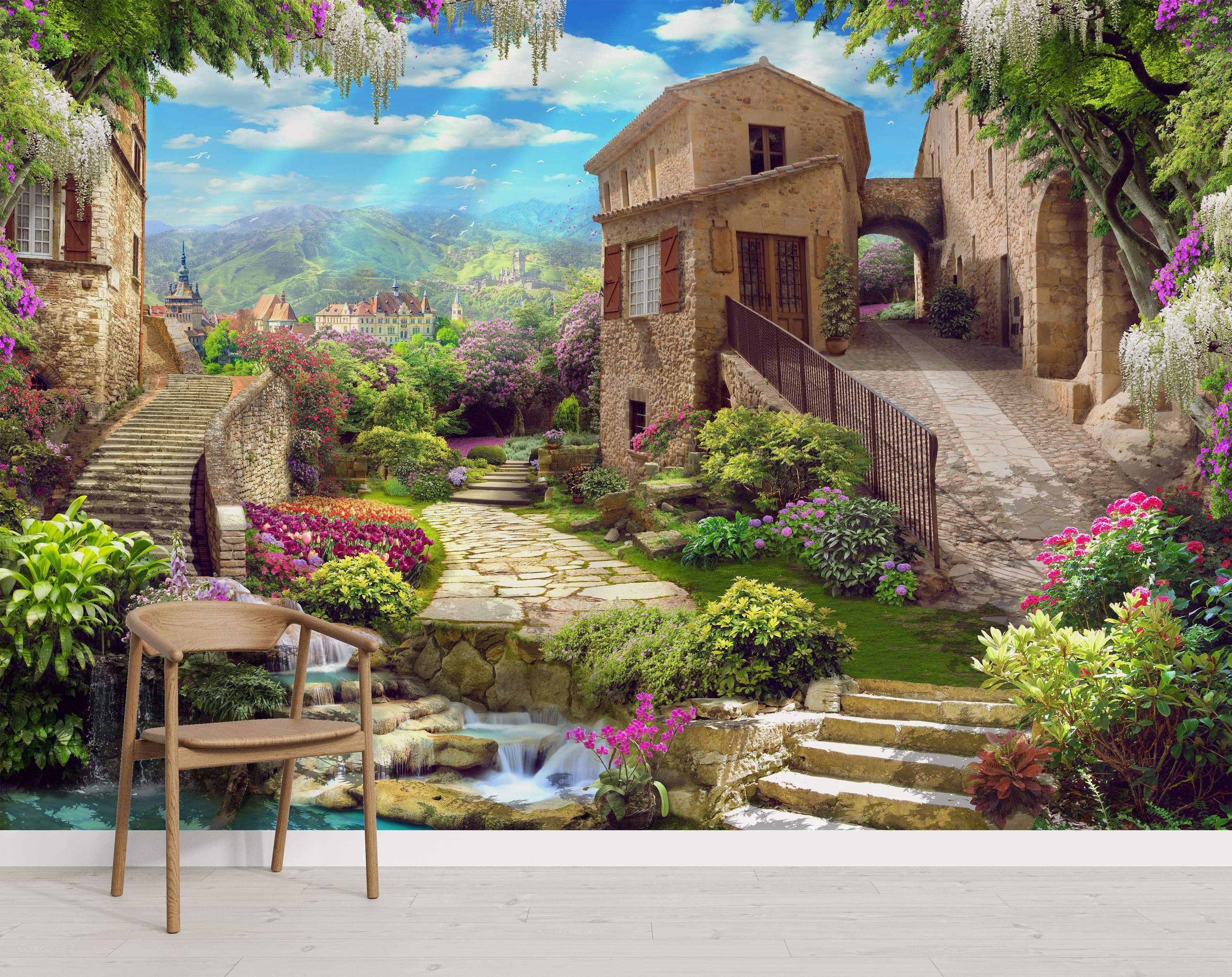 Mural depicting a sunlit Italian village with stone buildings, lush gardens, colorful flowers, stairs, a waterfall, and mountains.