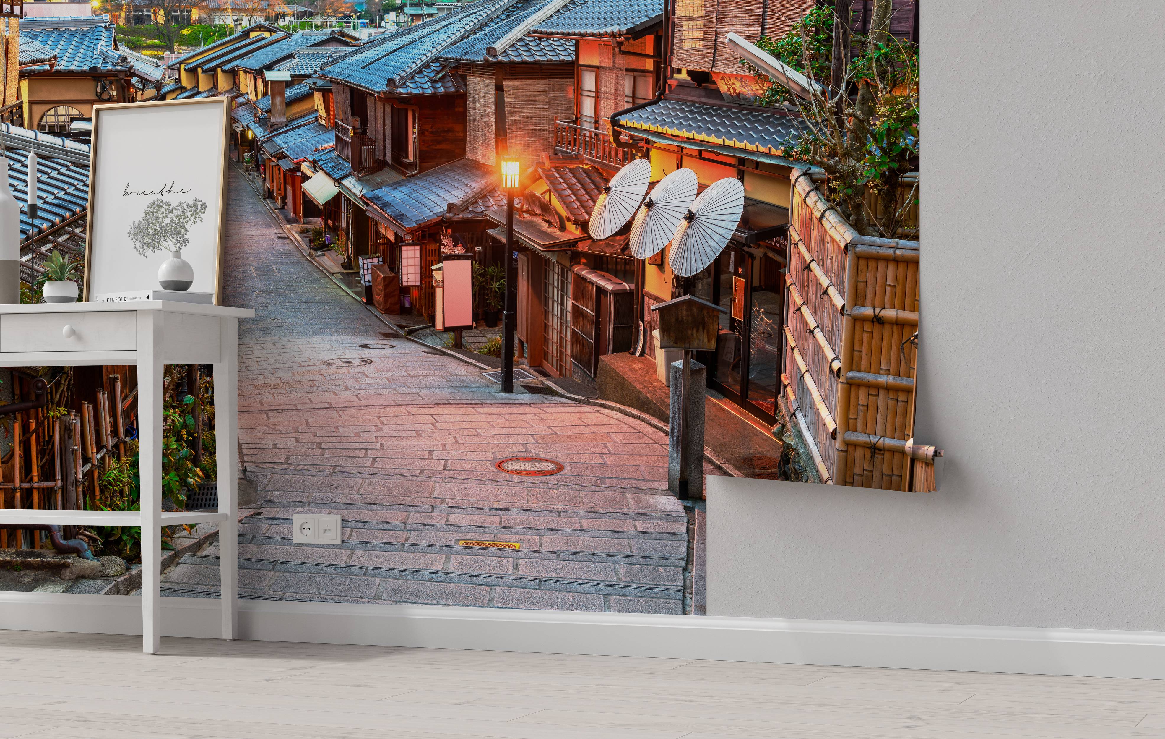 A mural of a narrow, sloping cobblestone street in a Japanese town at dusk, with glowing lanterns and traditional tiled-roof houses.