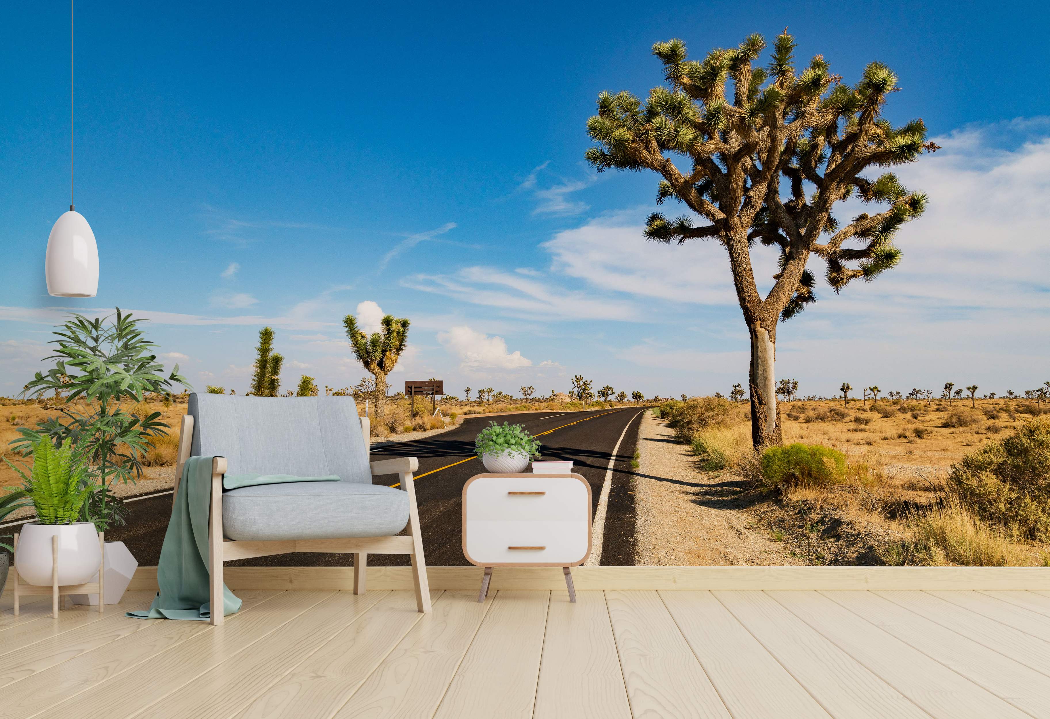 Mural of a desert highway curving past large Joshua trees under a bright blue sky in a sunny, arid landscape.