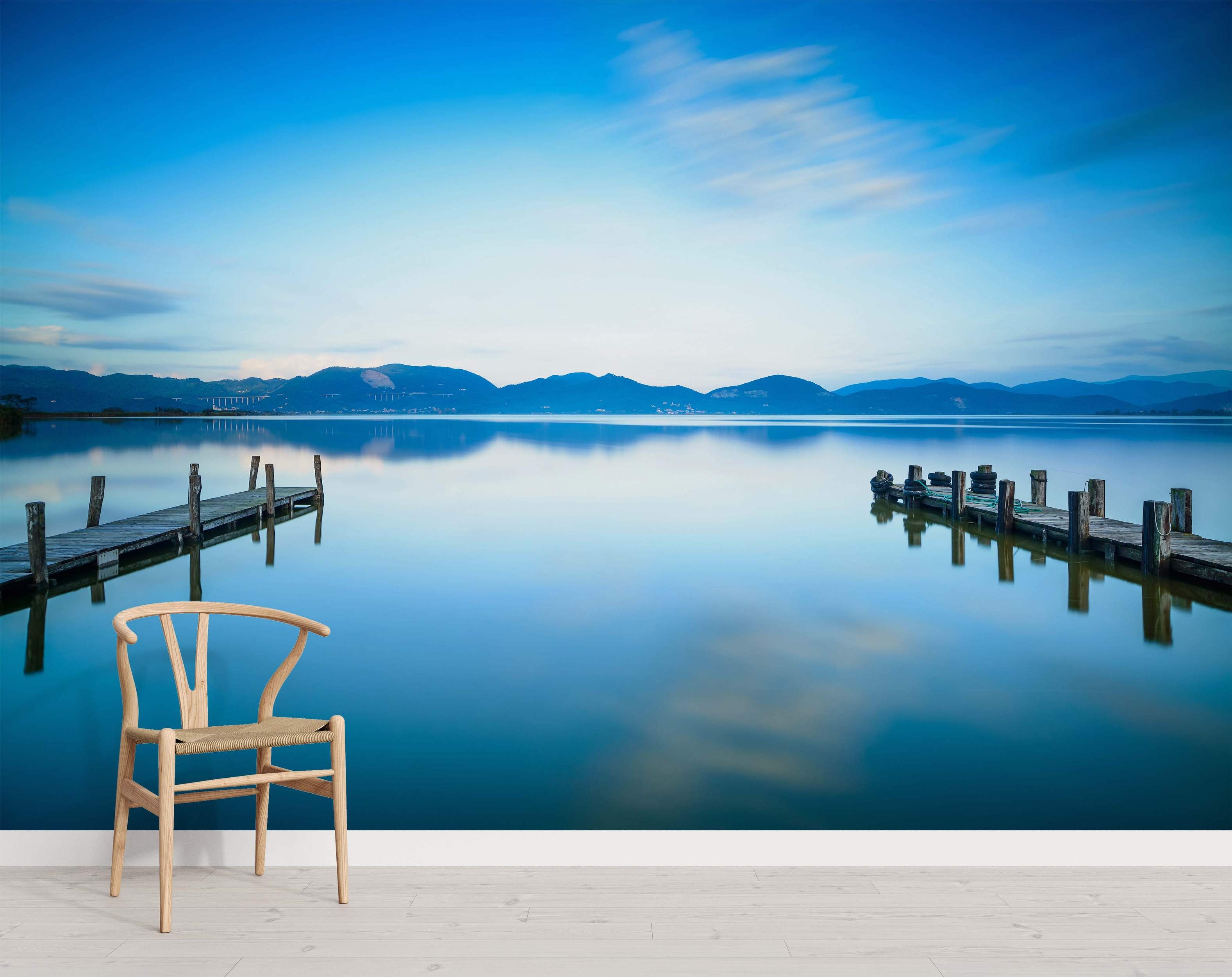Photographic mural depicting a serene blue lake with two wooden docks reflecting in the calm water under distant mountains.