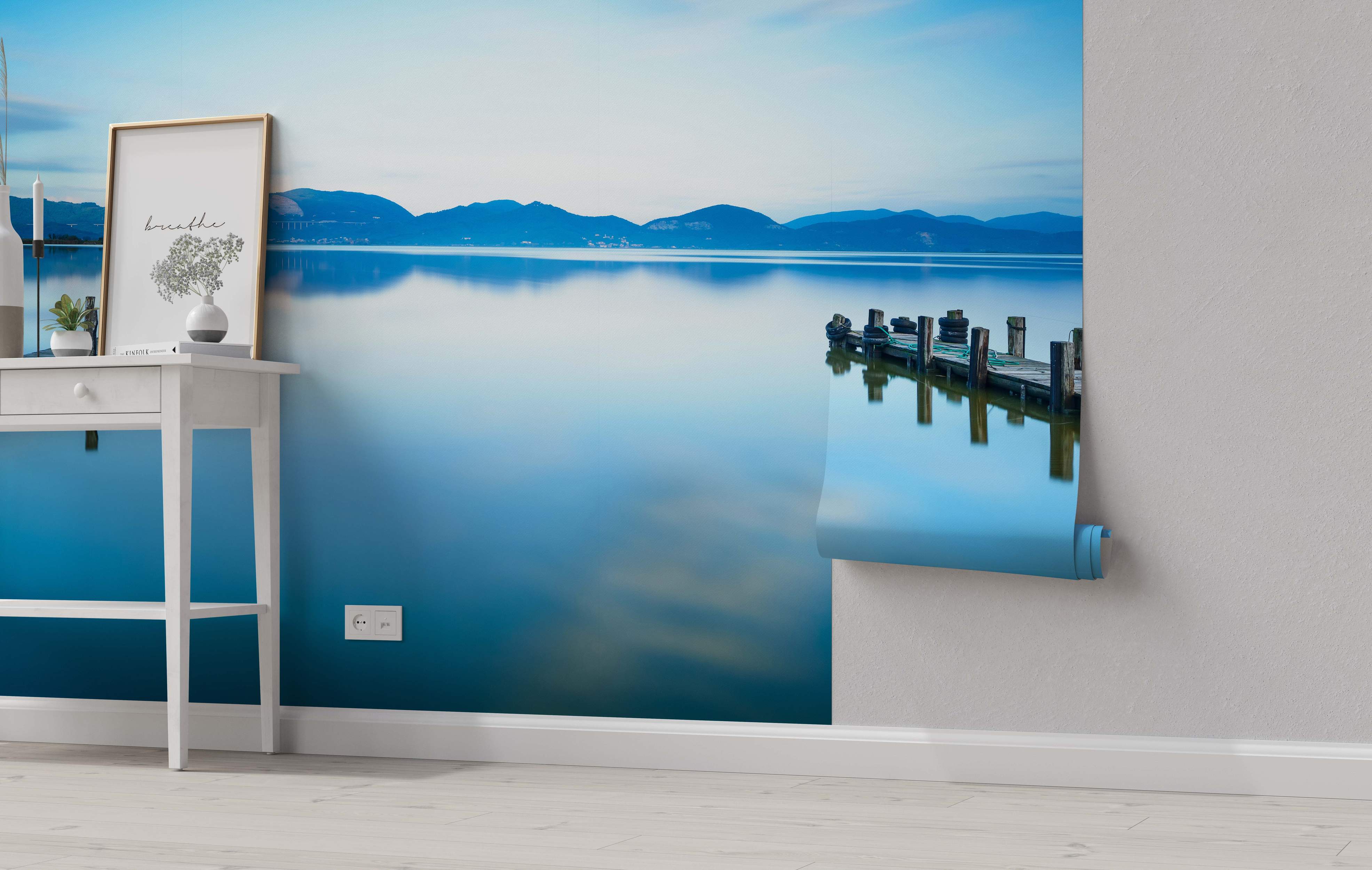 Tranquil lake mural depicting distant blue mountains reflecting in calm water with a wooden dock on the right.