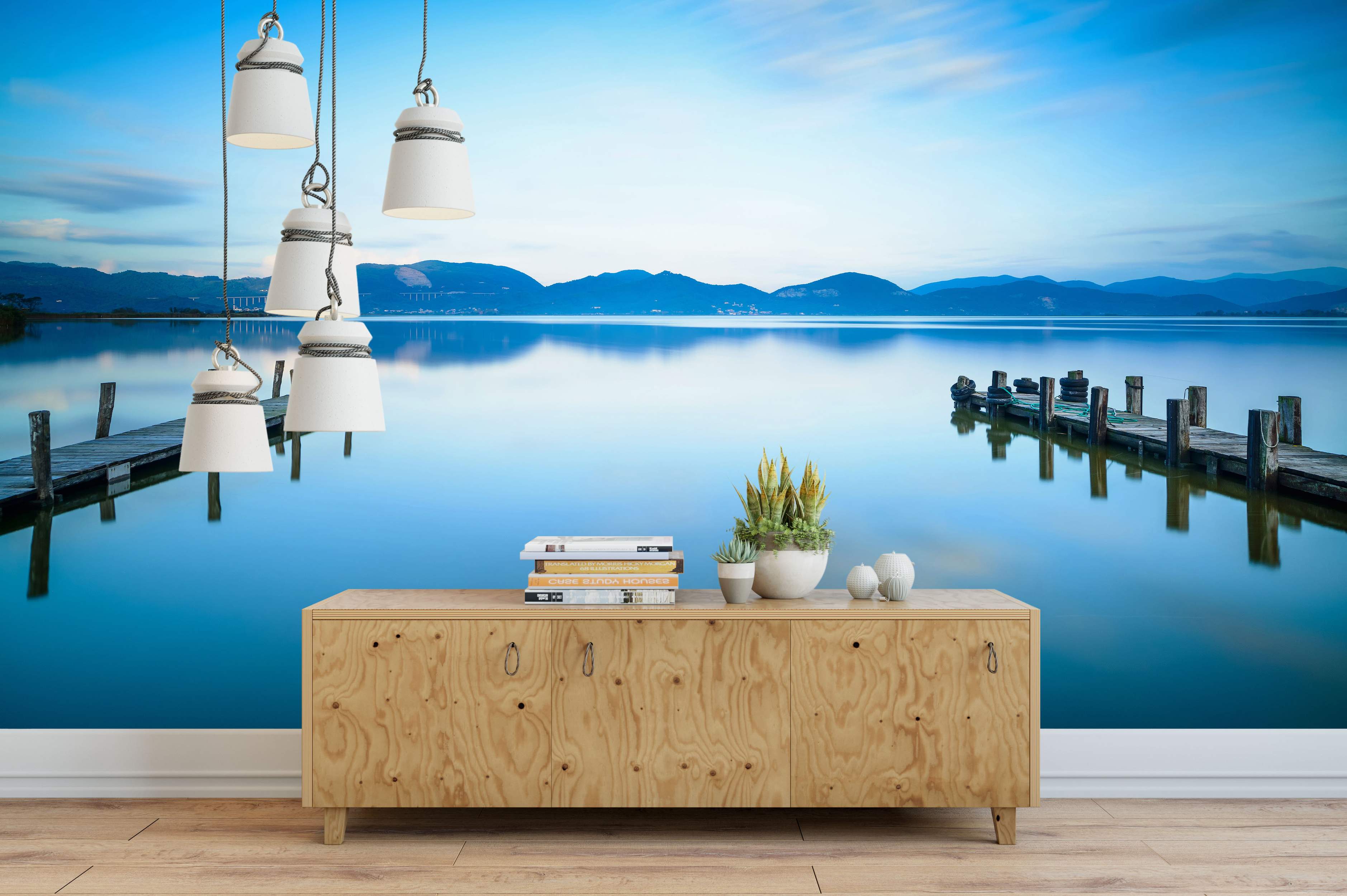 Mural featuring a tranquil blue lake reflecting mountains and sky, with two weathered wooden piers extending into the water.