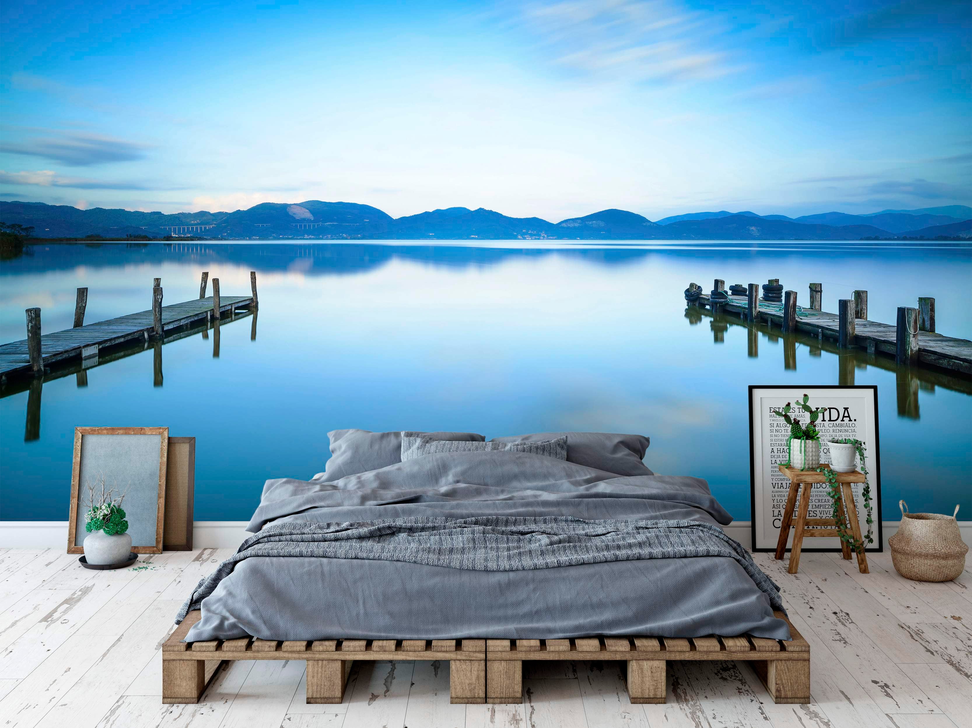 Photorealistic mural depicting a tranquil blue lake with wooden docks, water reflections, and distant mountains under a soft sky.