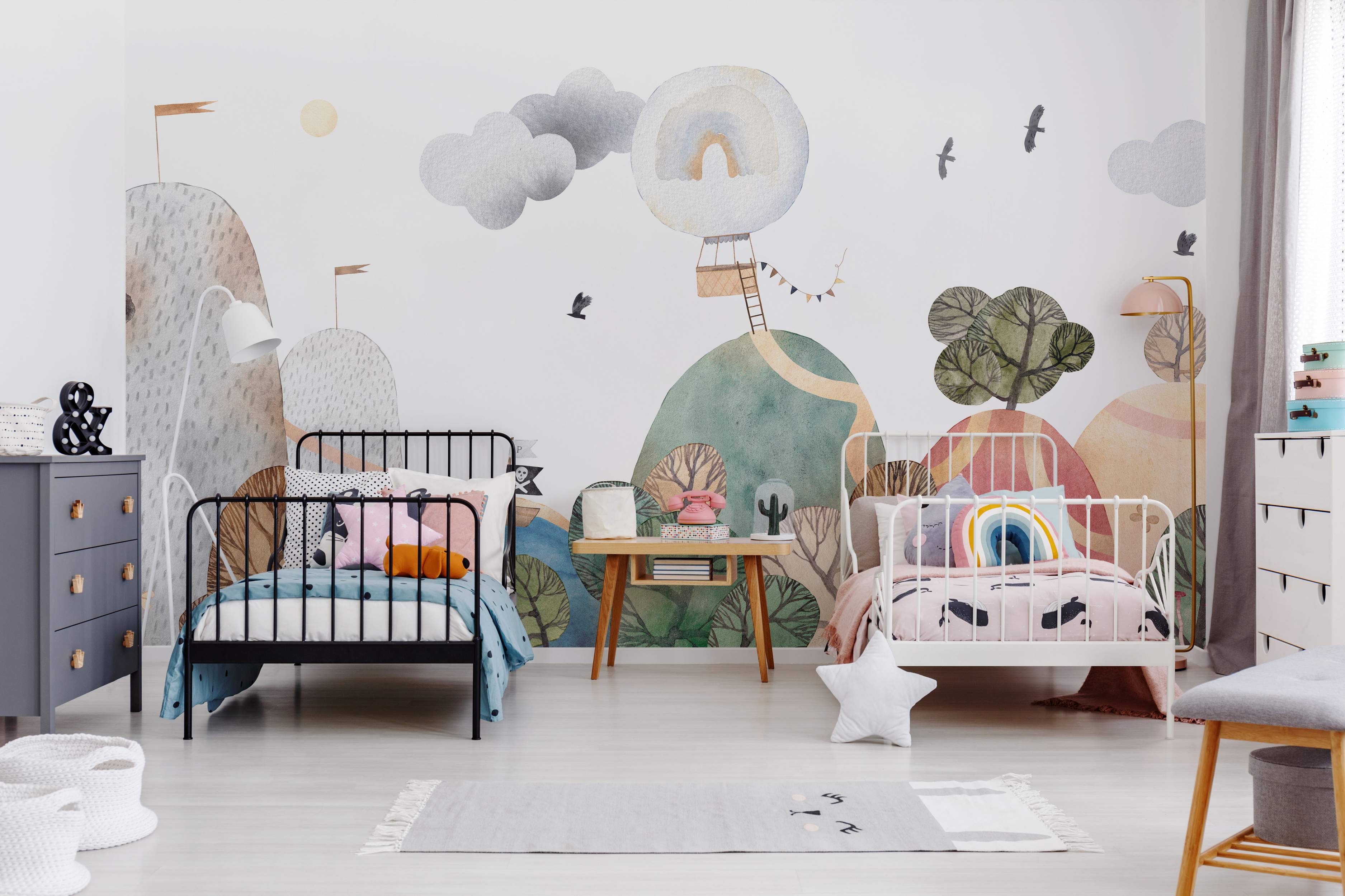 Whimsical watercolor mural featuring pastel hills, clouds, birds, and a hot air balloon with a rainbow.
