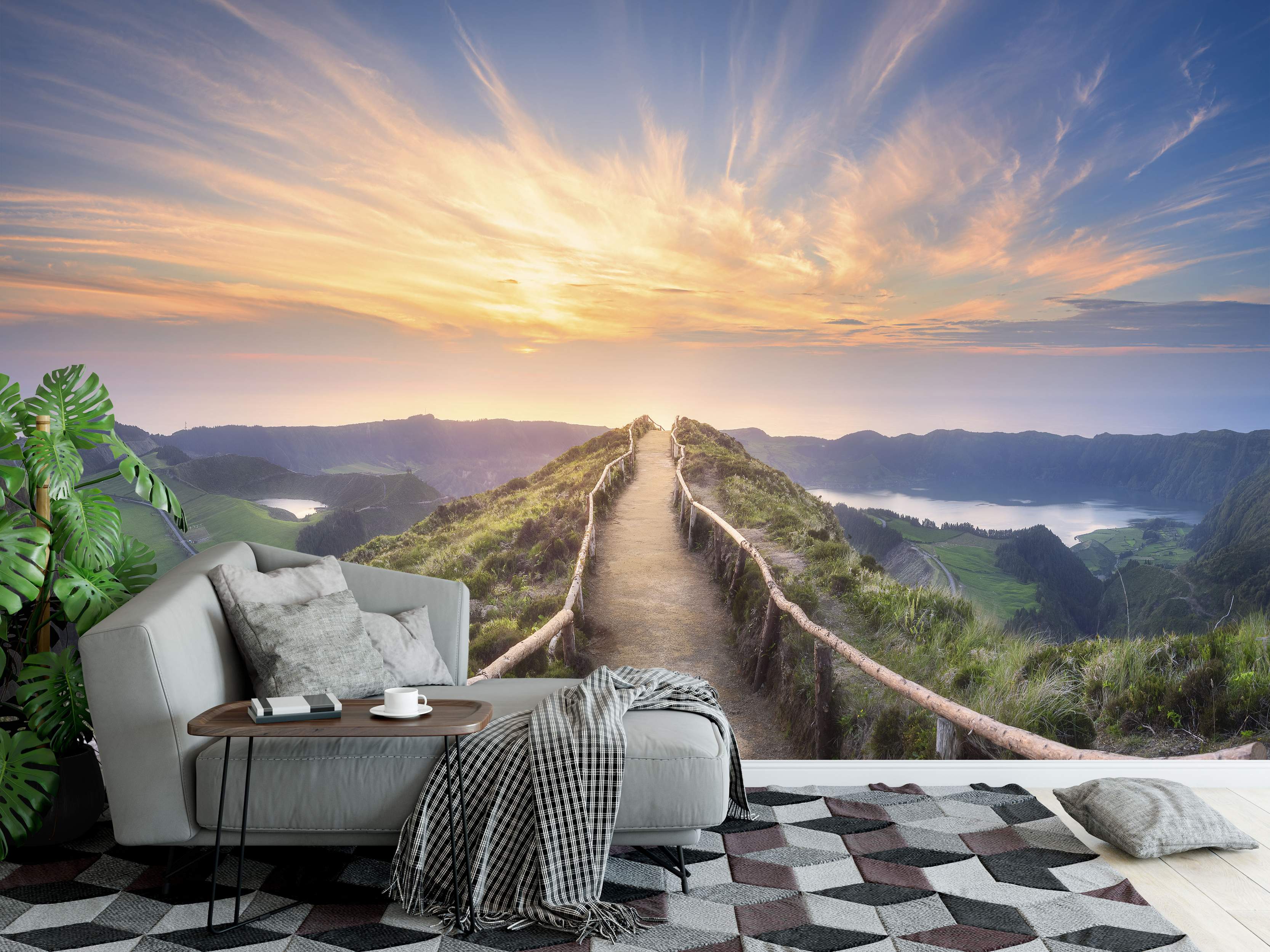 Scenic mural featuring a dirt path along a mountain ridge, overlooking lakes and valleys under a vibrant orange sunset sky.