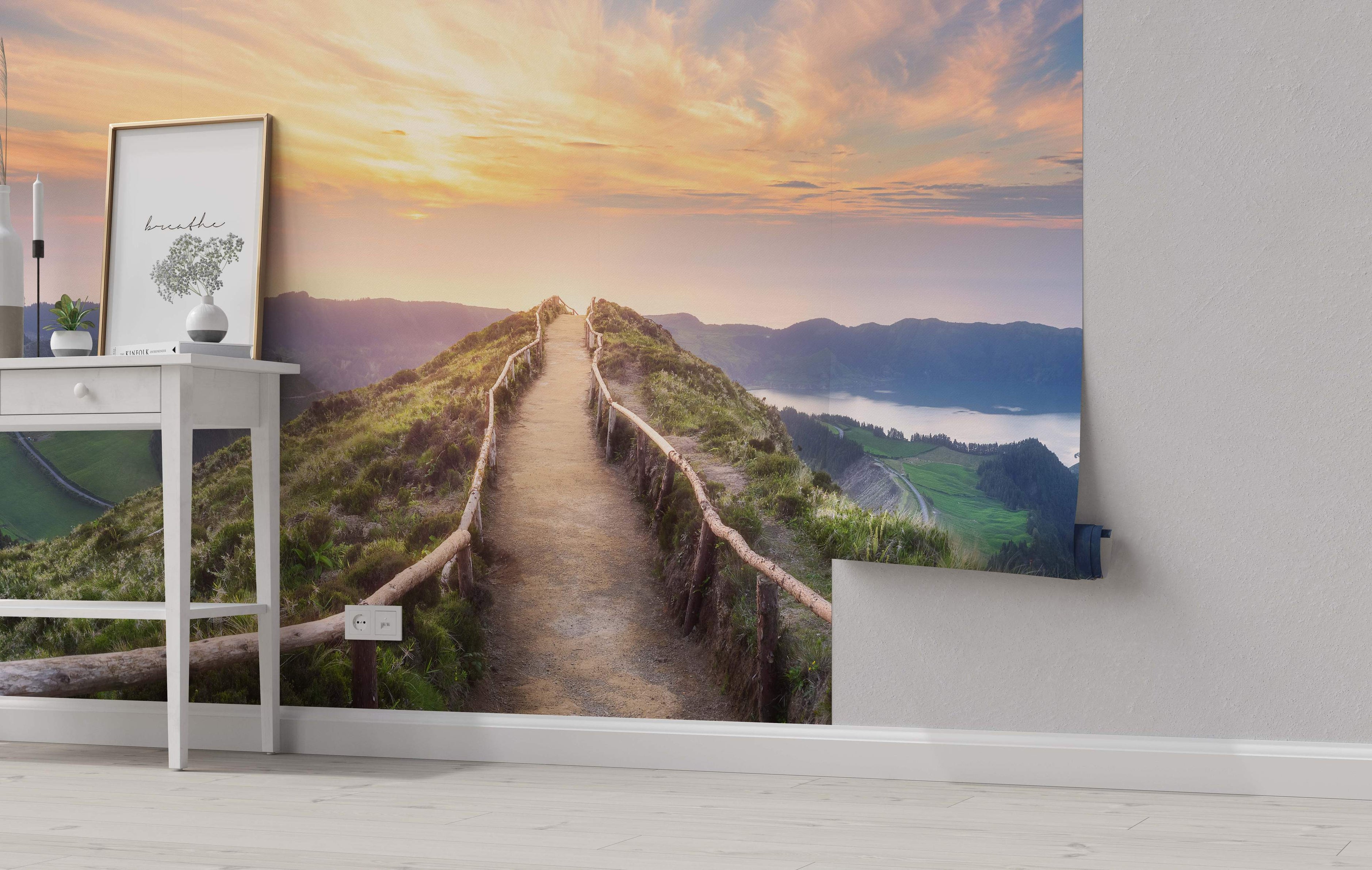 Scenic mural of a dirt path on a green mountain ridge overlooking a lake and valleys under a warm sunset sky.