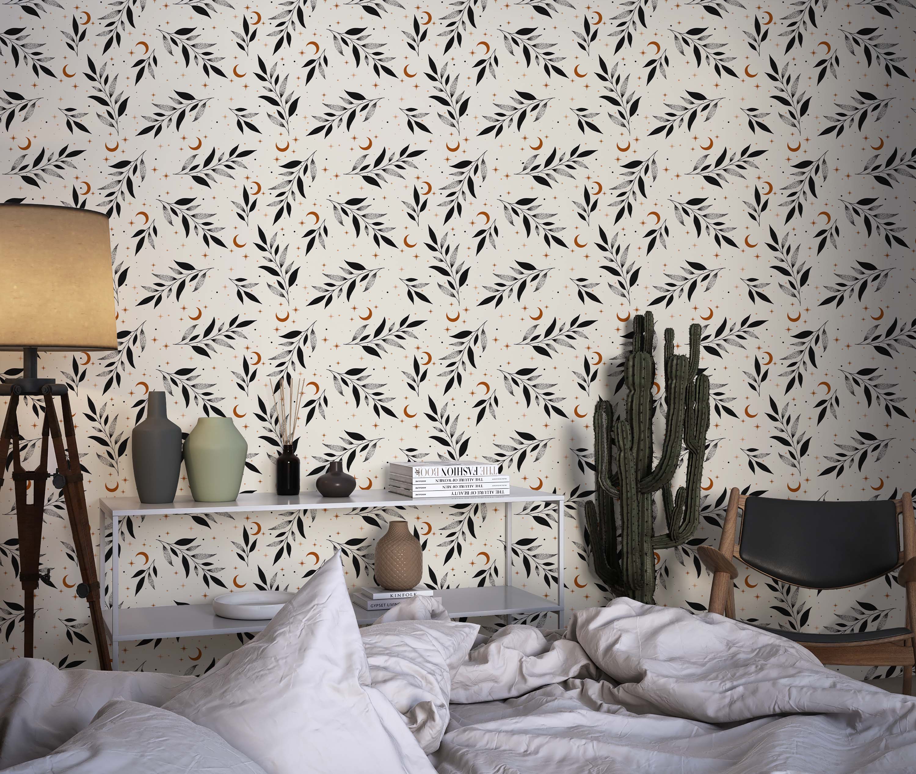 A celestial wallpaper with black leaf sprigs, some solid and some stippled, with orange crescent moons and stars on a cream base.