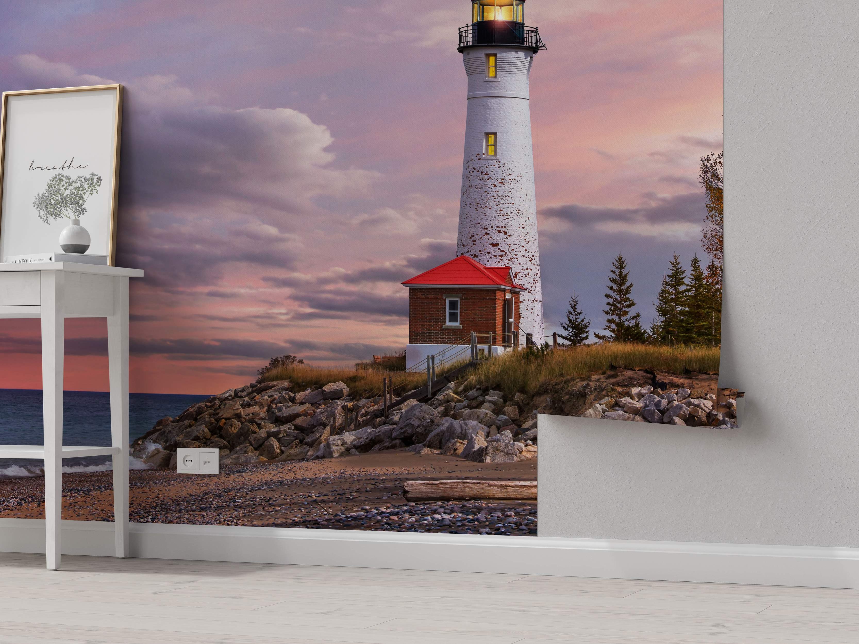 Mural depicting a white lighthouse on a rocky shore beside a pebble beach, under a vibrant pink and purple sunset sky.