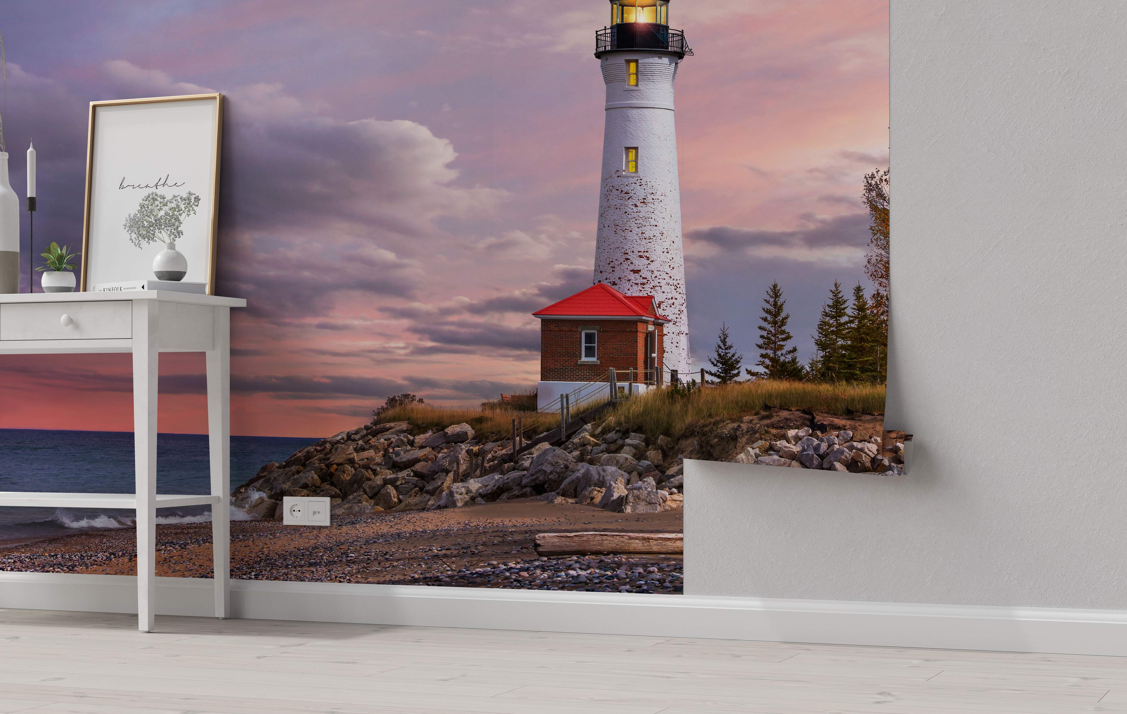 Mural depicting a white lighthouse on a rocky shore beside a pebble beach, under a vibrant pink and purple sunset sky.