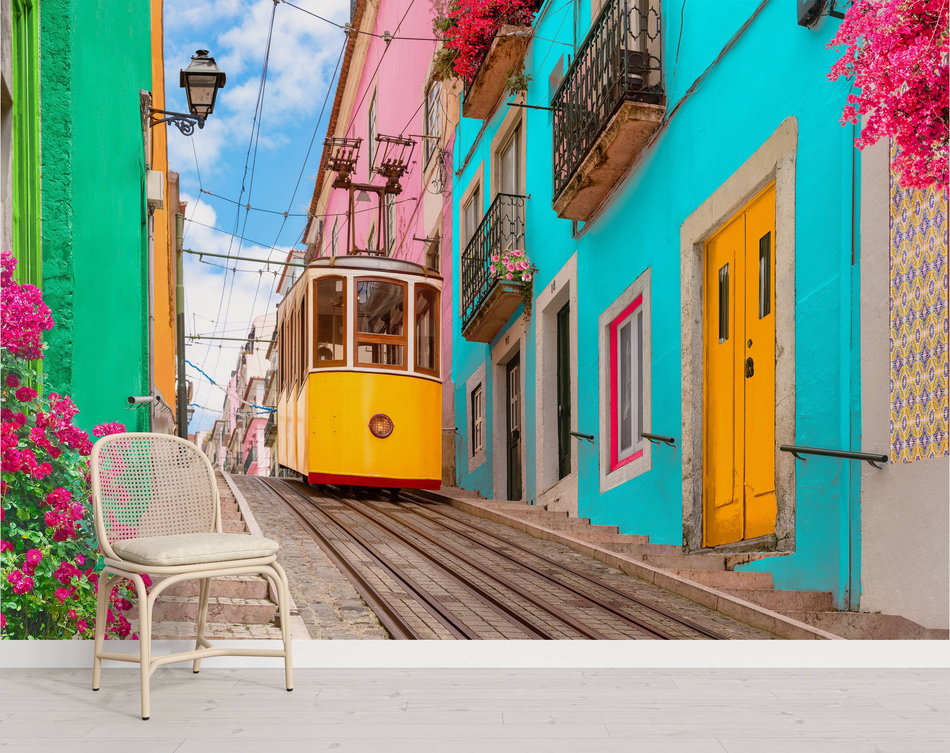 Mural of a yellow tram on a steep, narrow street flanked by vibrant green, pink, and turquoise buildings under a blue sky.