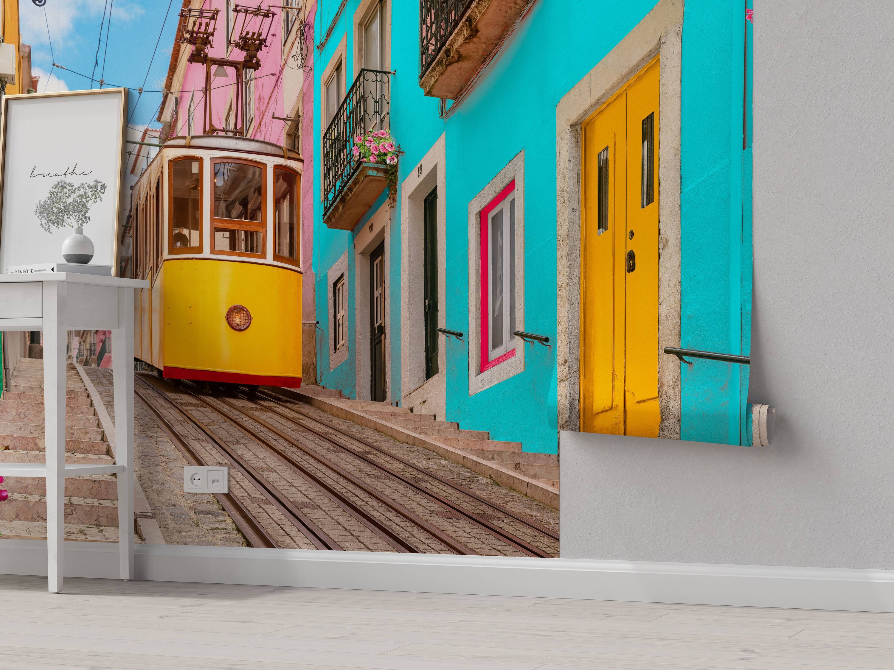 A photographic mural of a yellow tram on a steep street flanked by vibrant cyan, pink, and green buildings under a blue sky.
