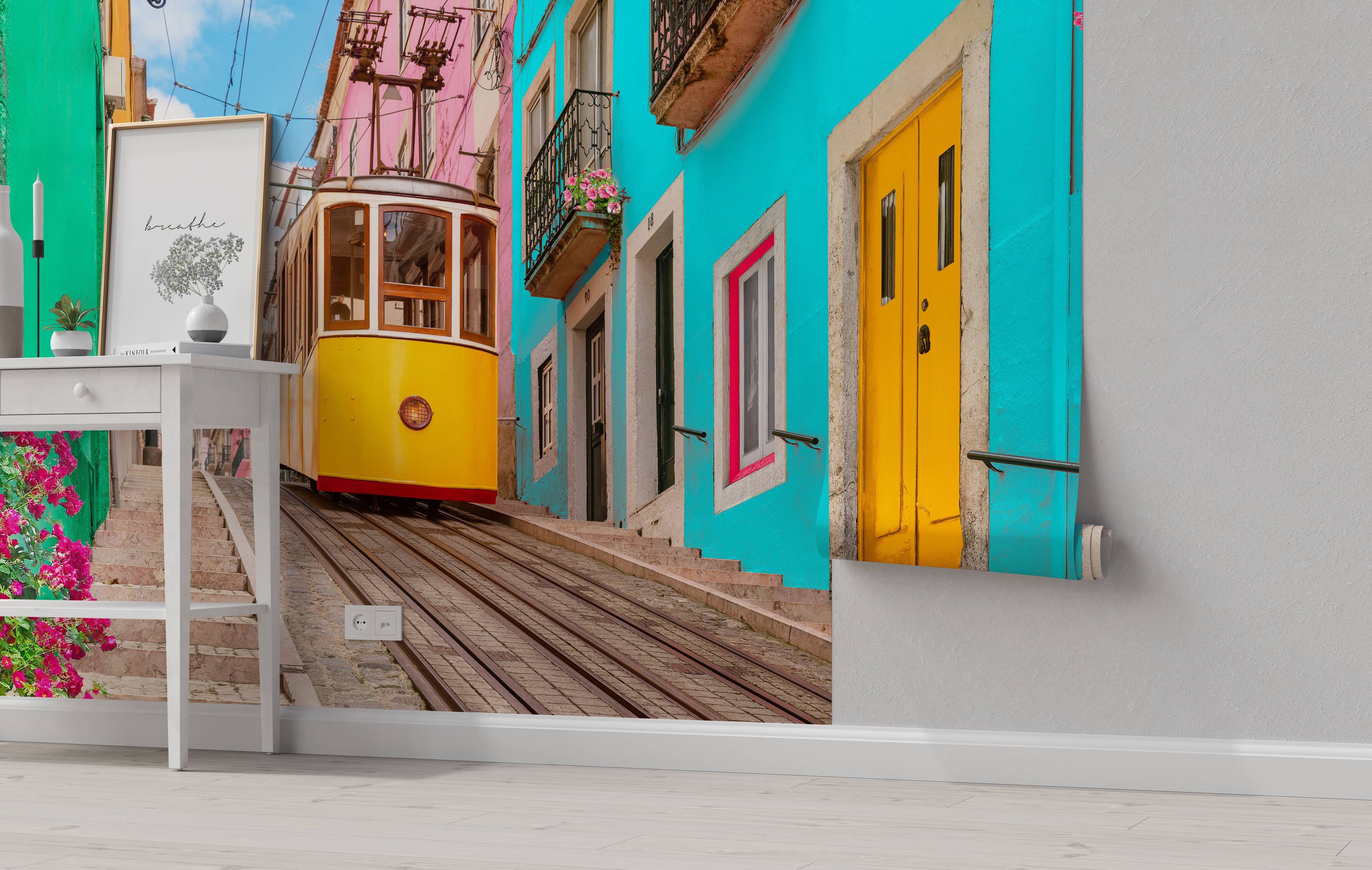 A photographic mural of a yellow tram on a steep street flanked by vibrant cyan, pink, and green buildings under a blue sky.