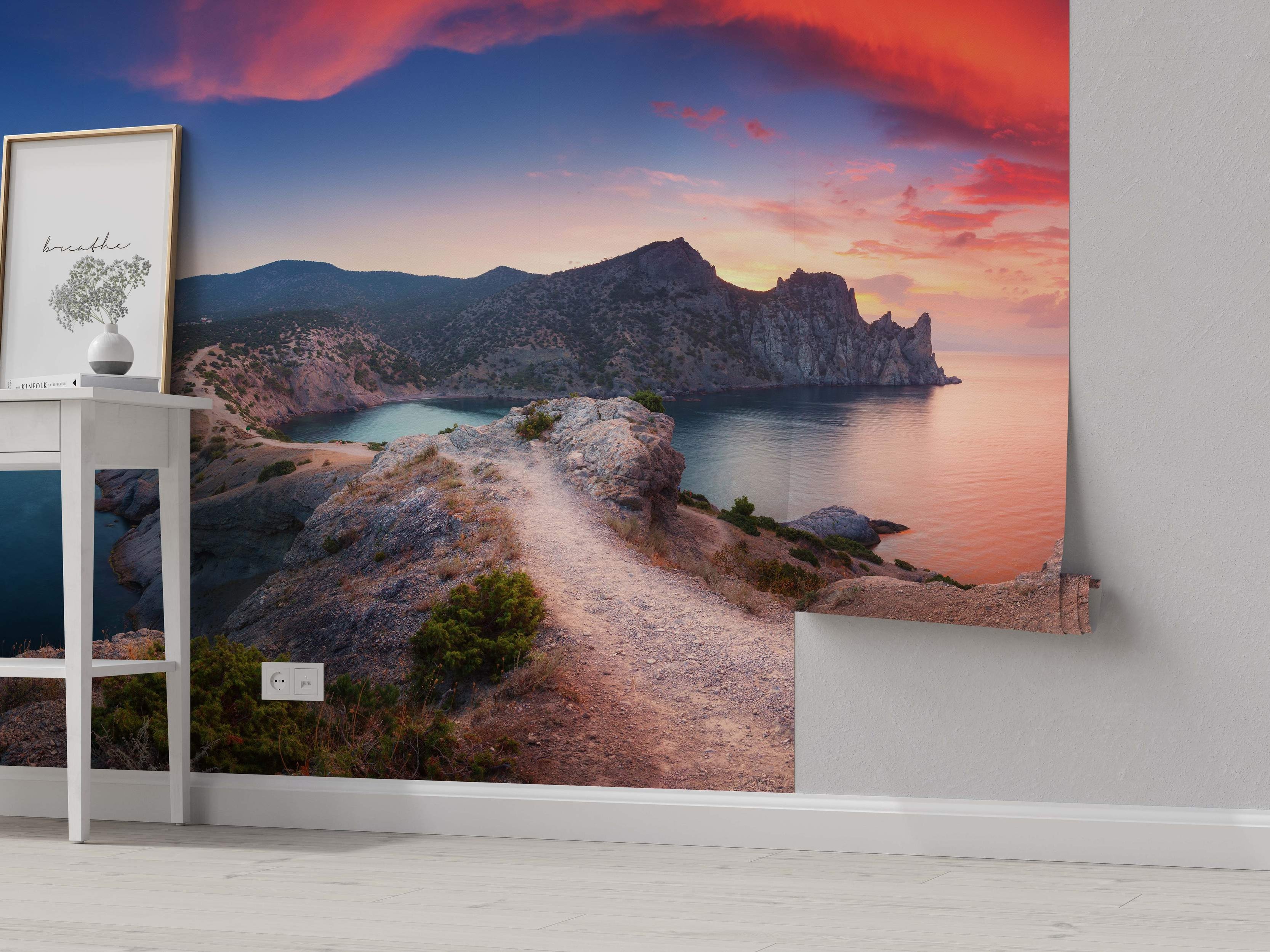 Mural depicting a dramatic coastal mountain landscape at sunset, with a path winding along a cliff overlooking the sea.