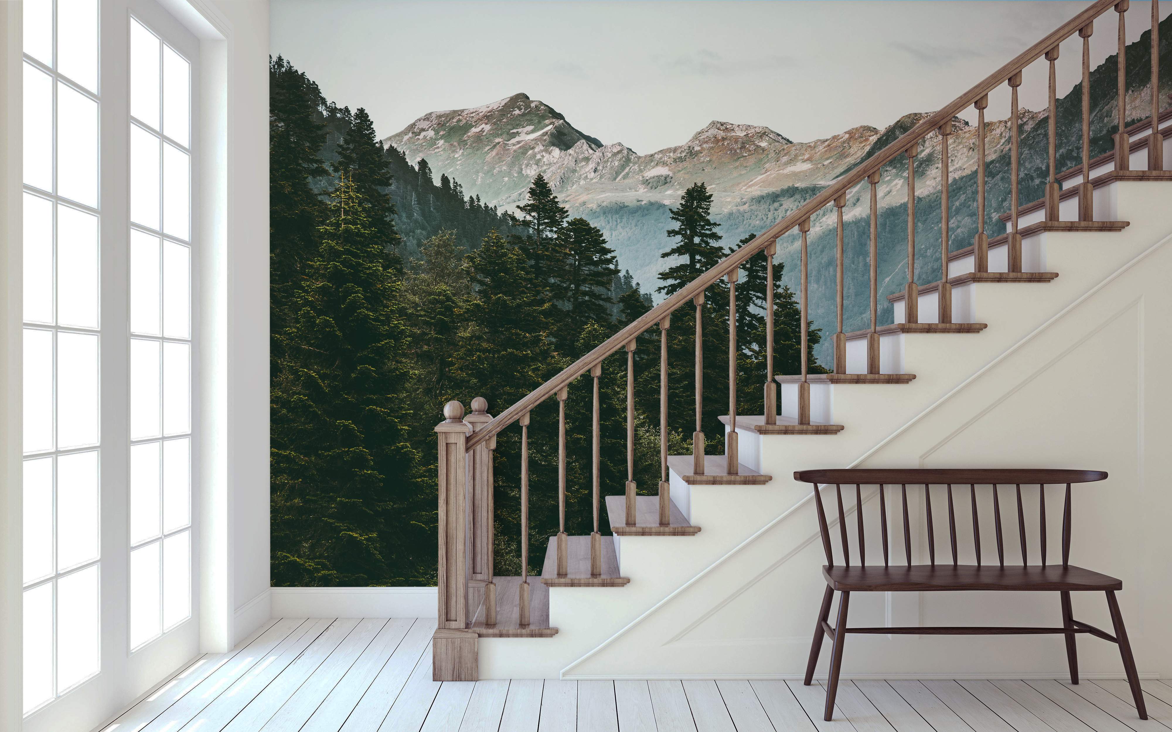 Scenic mountain landscape mural featuring snow-dusted peaks above a dense green pine forest under a pale sky.