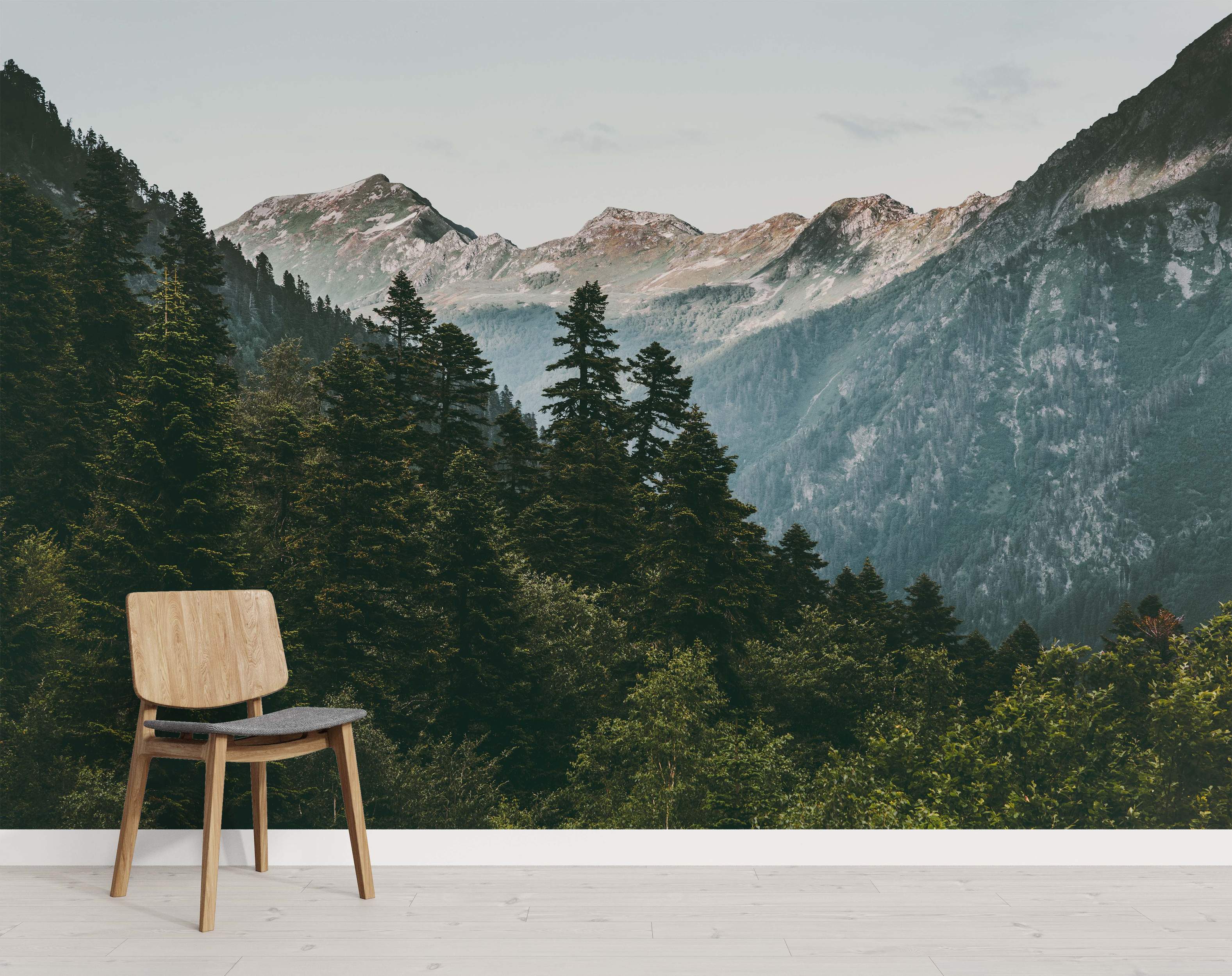 Mural depicting a vast mountain range with lush green pine forests below rocky peaks under a soft sky.